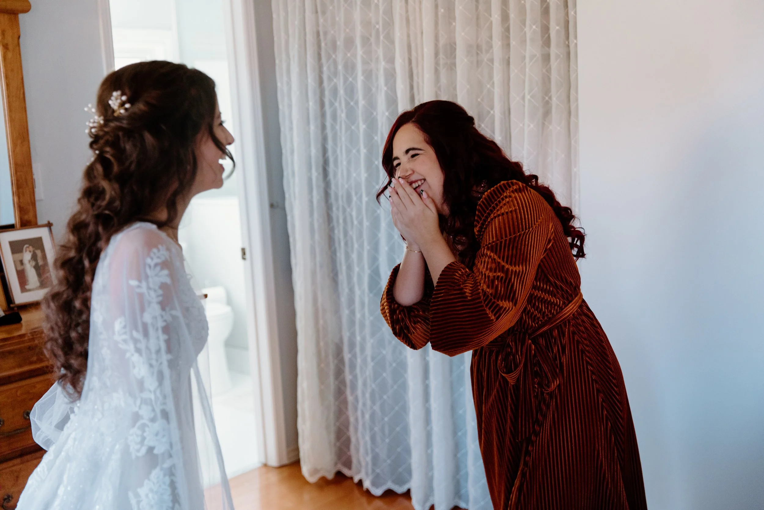 Candid photo of a bride doing a dress reveal with her overjoyed maid of honour on her Toronto wedding morning