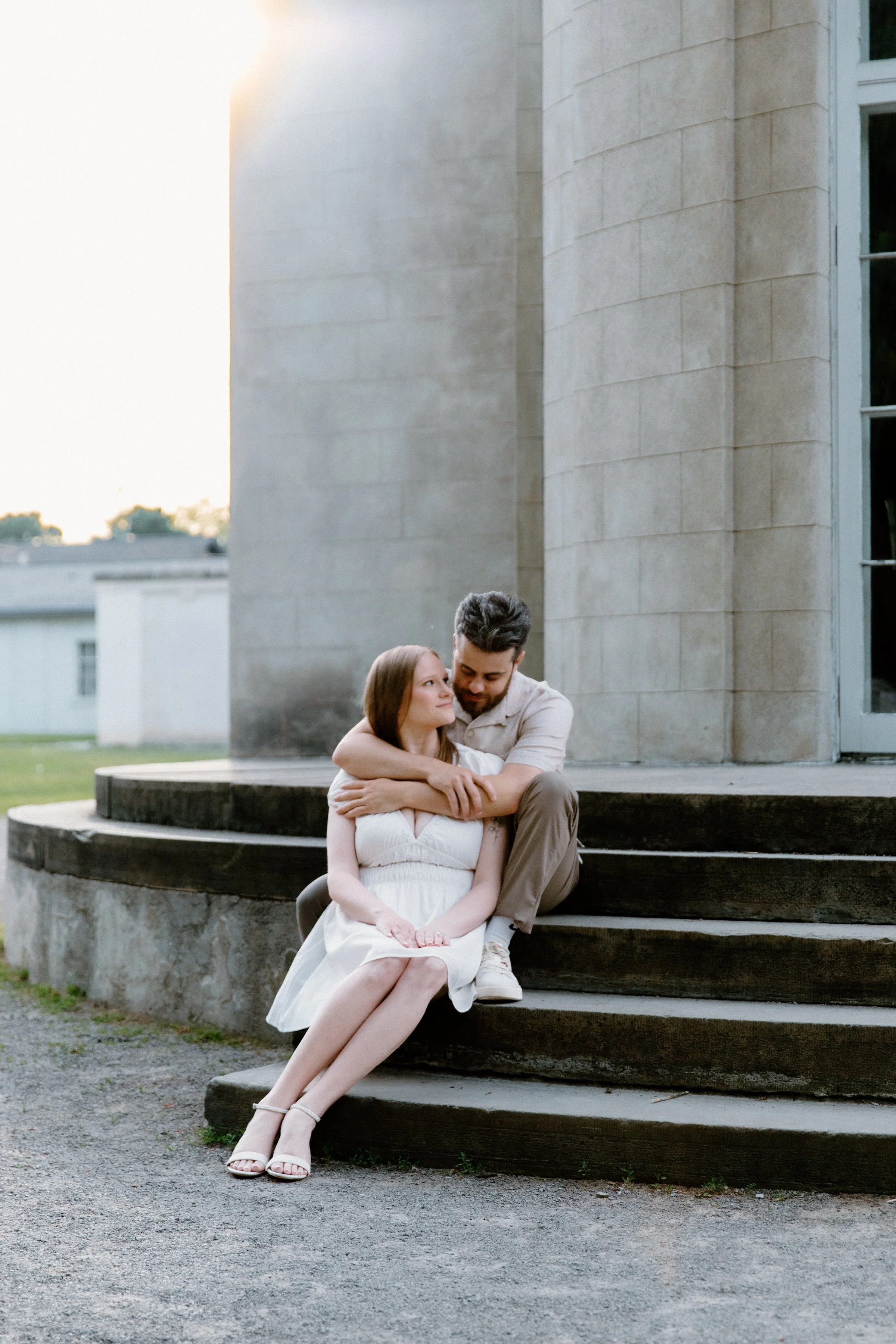 Stylish couple sitting together on the steps of Dundurn Castle embracing during their engagement session