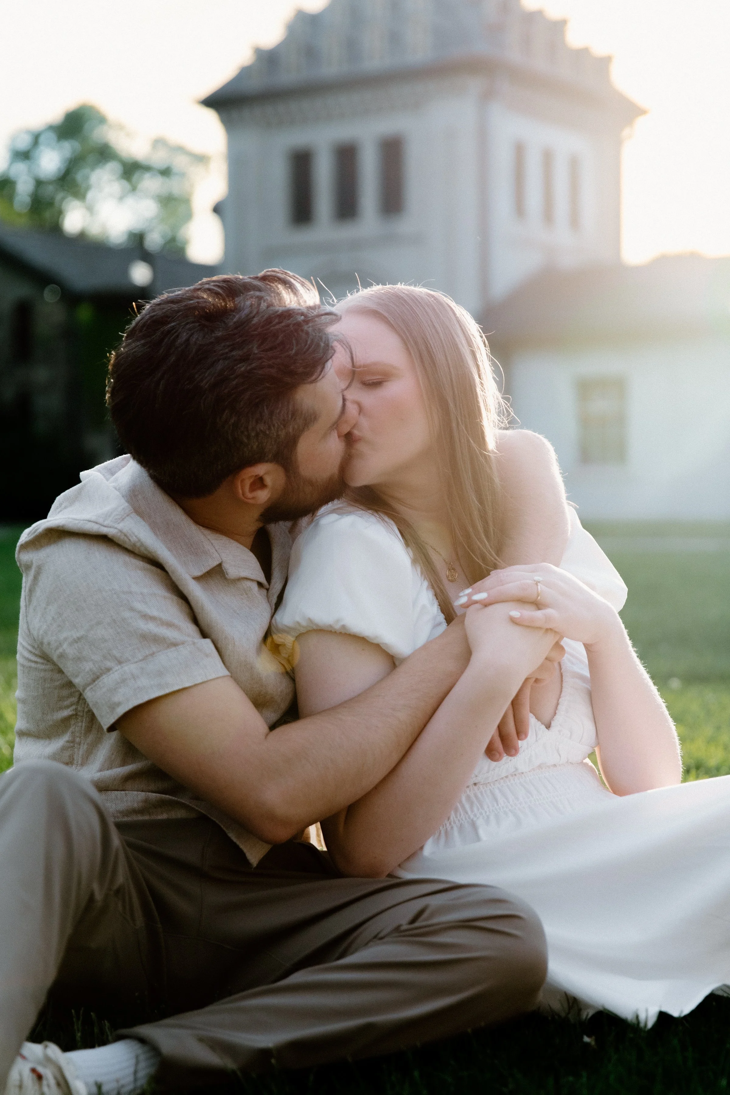 Romantic photo of a couple kissing while seated on the lawn at Dundurn Castle with the sunset glowing behind them