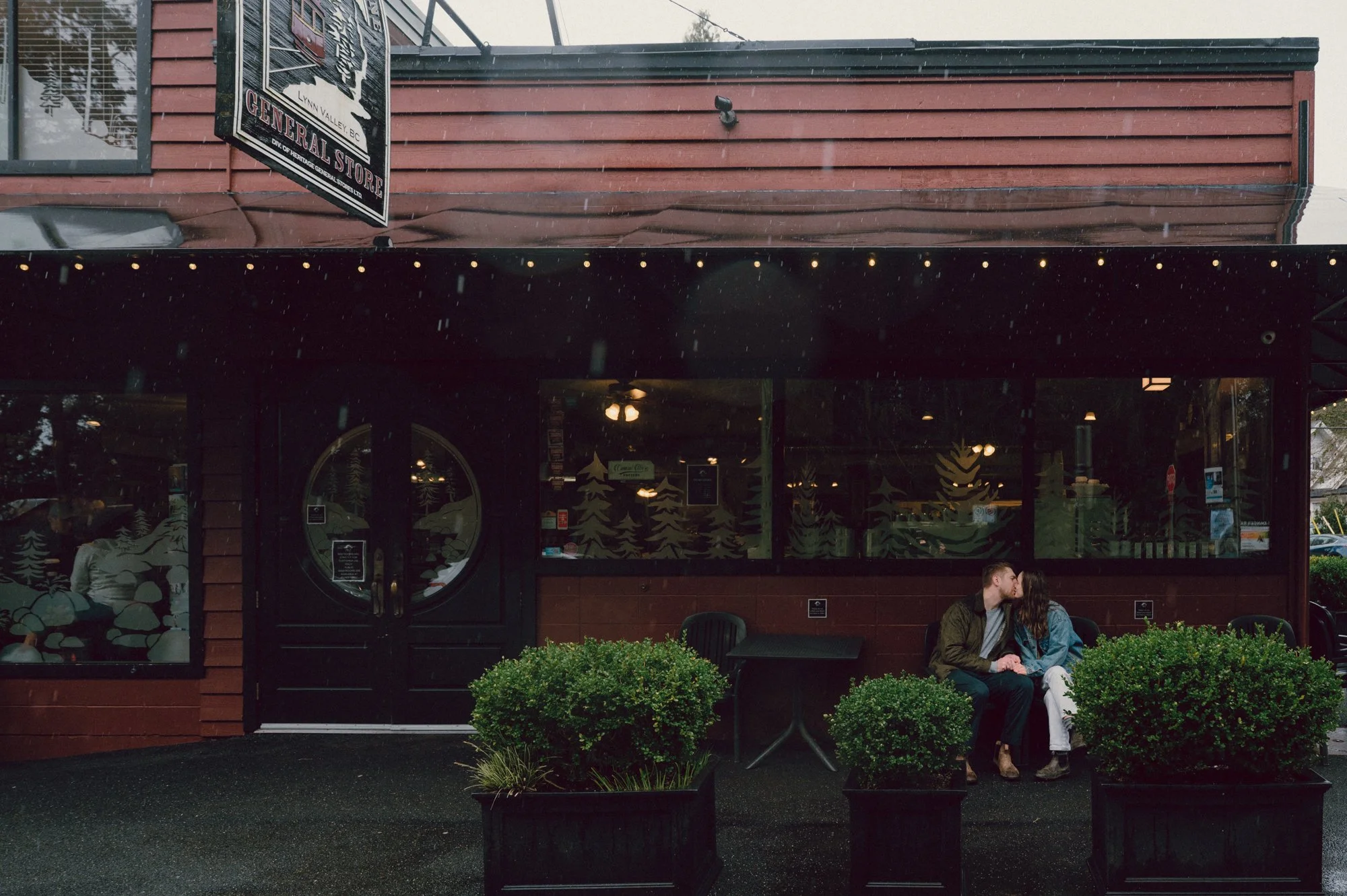 Editorial inspired photo of a couple sharing a kiss under the awning of the End of the Line General Store in Lynn Valley, North Vancouver on a rainy day