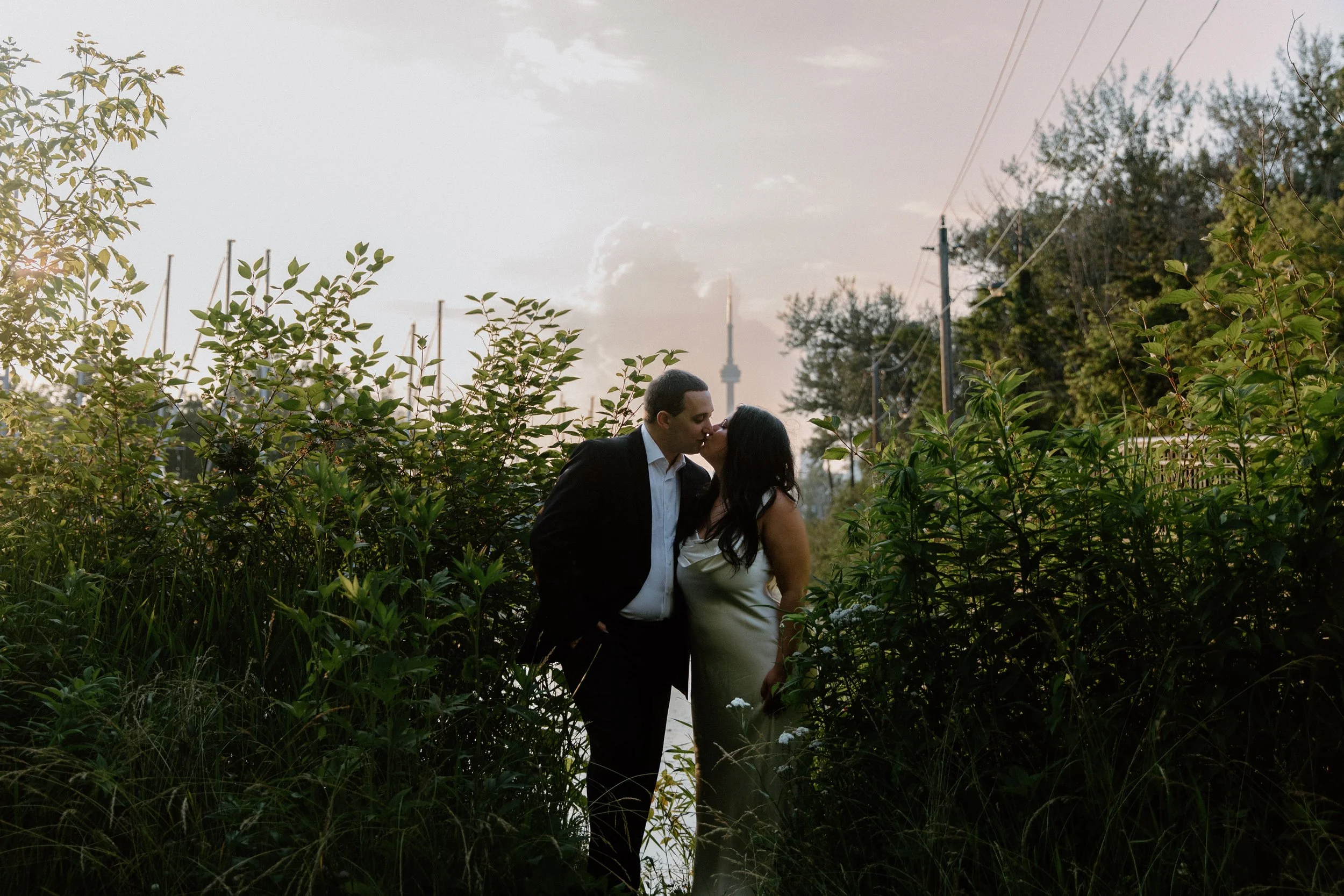 Editorial wedding portraits of a couple standing in a garden at sunset with the CN Tower in the background, Toronto