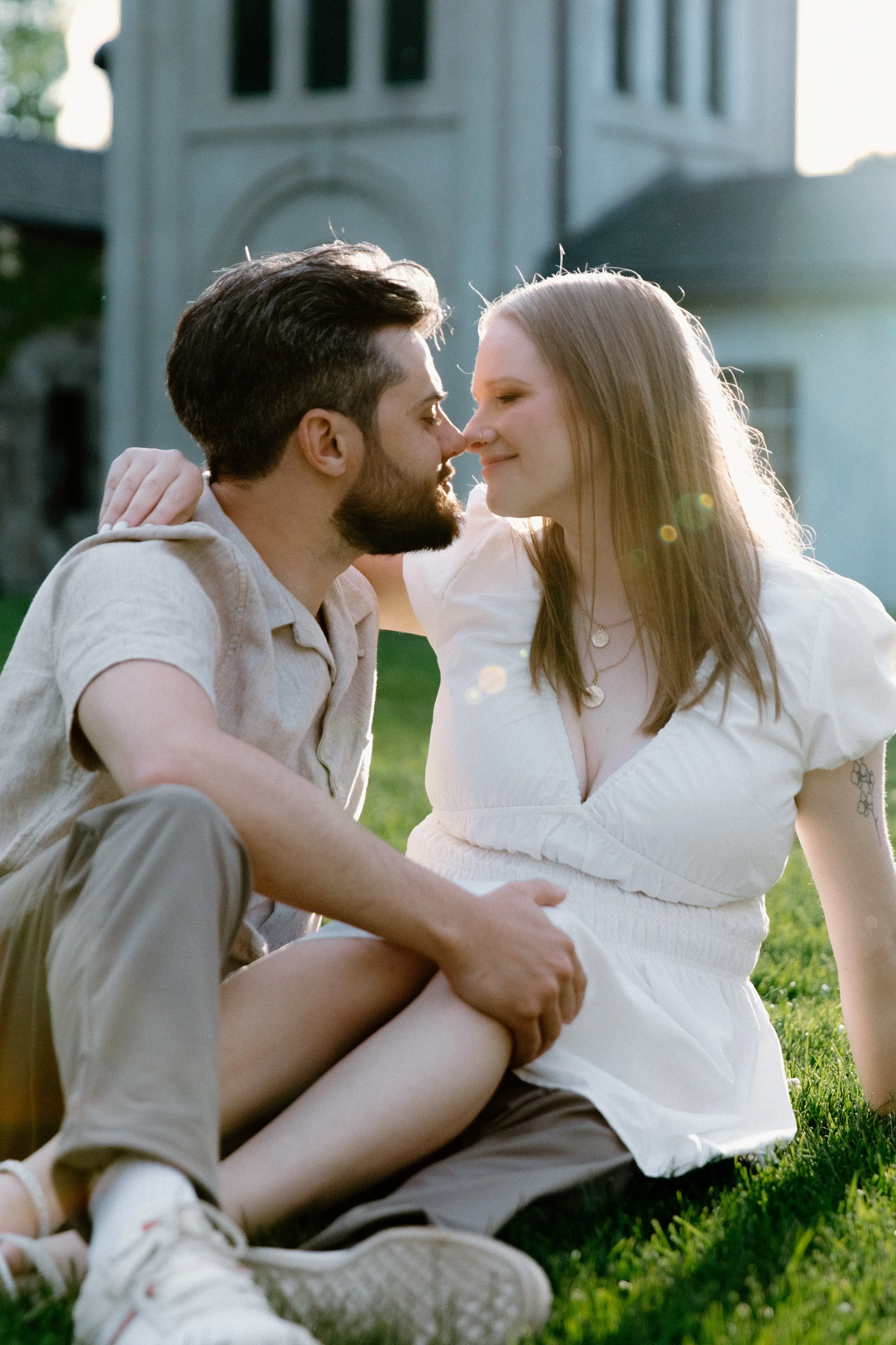 Stylish couple seated on the lawn embracing each other with the sunset behind them at Dundurn Castle, wearing a complementary neutral colour palette
