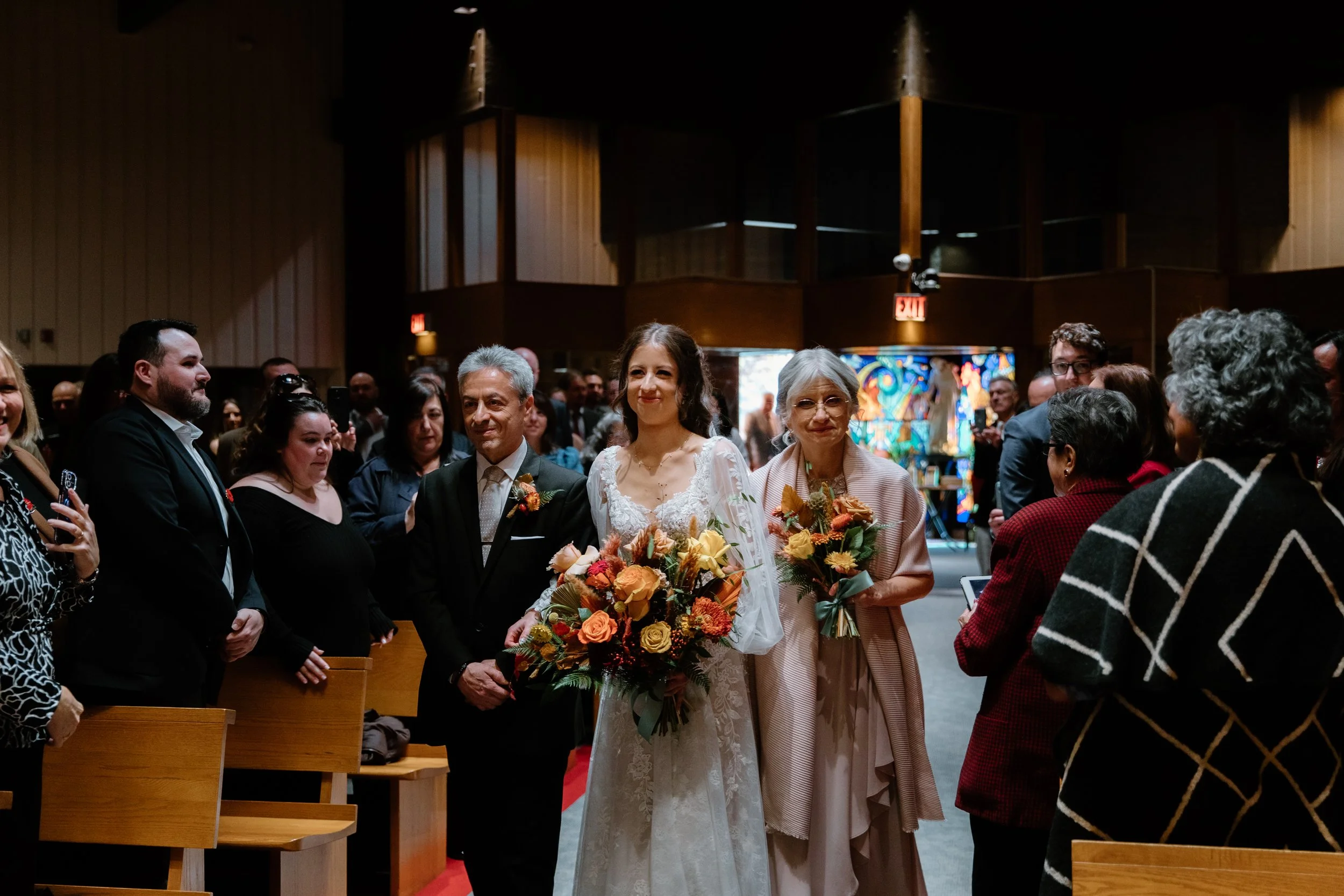 Documentary photo of a bride walking down the church aisle with her parents at her Toronto wedding