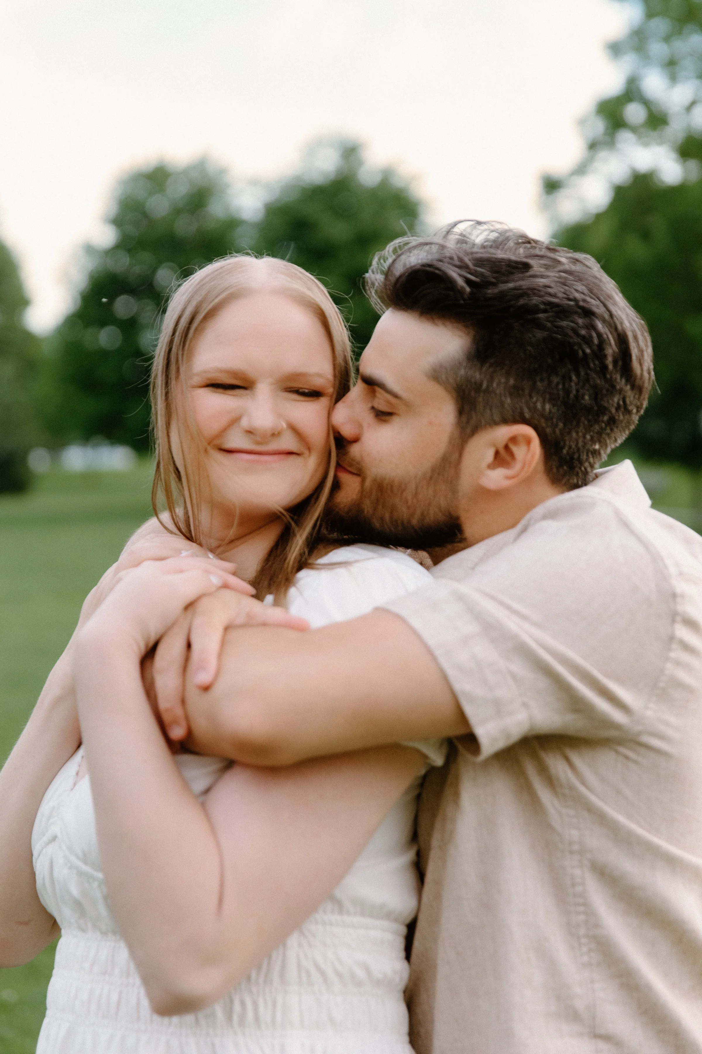 Romantic portrait of a couple embracing at Dundurn Castle as he kisses her on the cheek during their engagement session