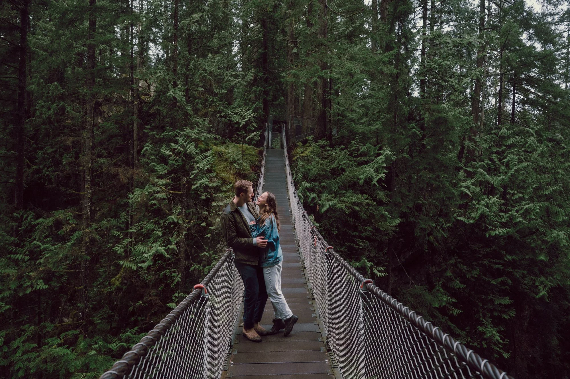 Wide romantic photo of a couple looking at each other on the Lynn Valley suspension bridge in North Vancouver