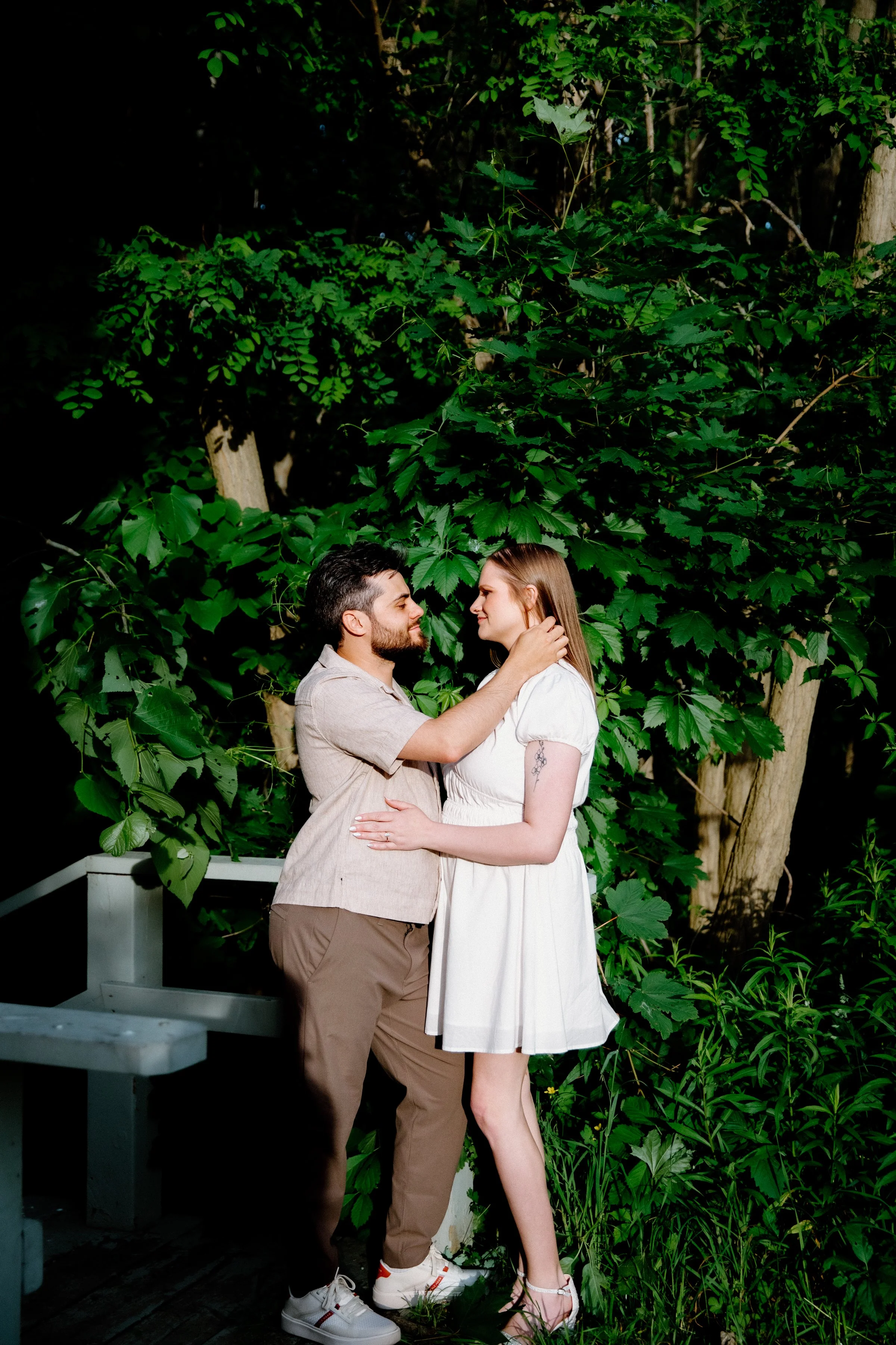 Dramatic editorial portrait of a couple standing against vibrant green foliage with direct sun on them at Dundurn Castle