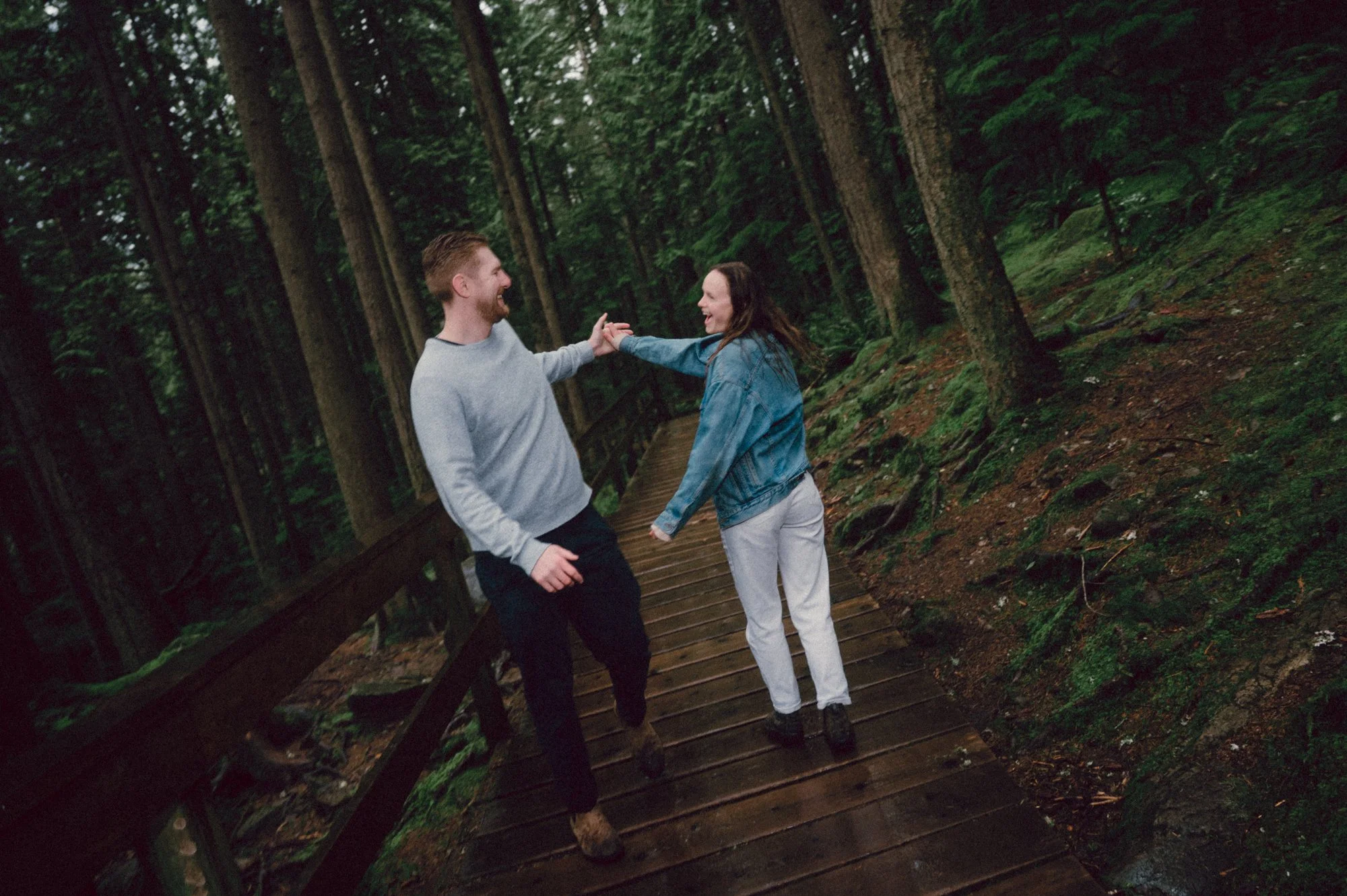 Editorial flash photo of a couple playfully dancing on a forest boardwalk during their engagement session in Lynn Valley, BC