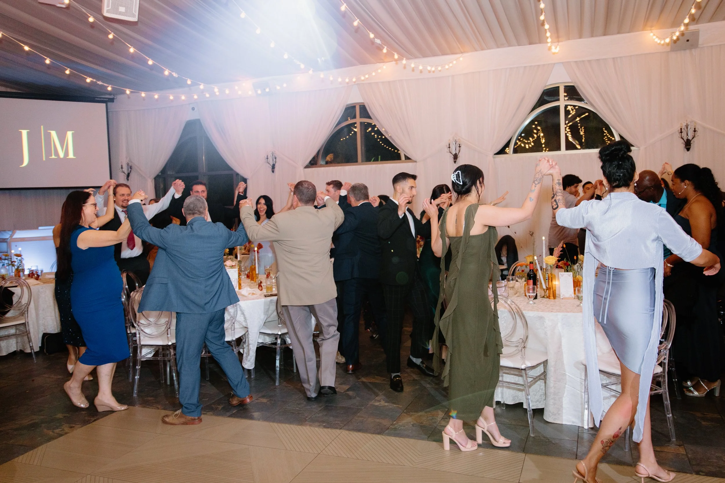 Wide energetic photo of guests dancing around their tables at a Caledon wedding reception
