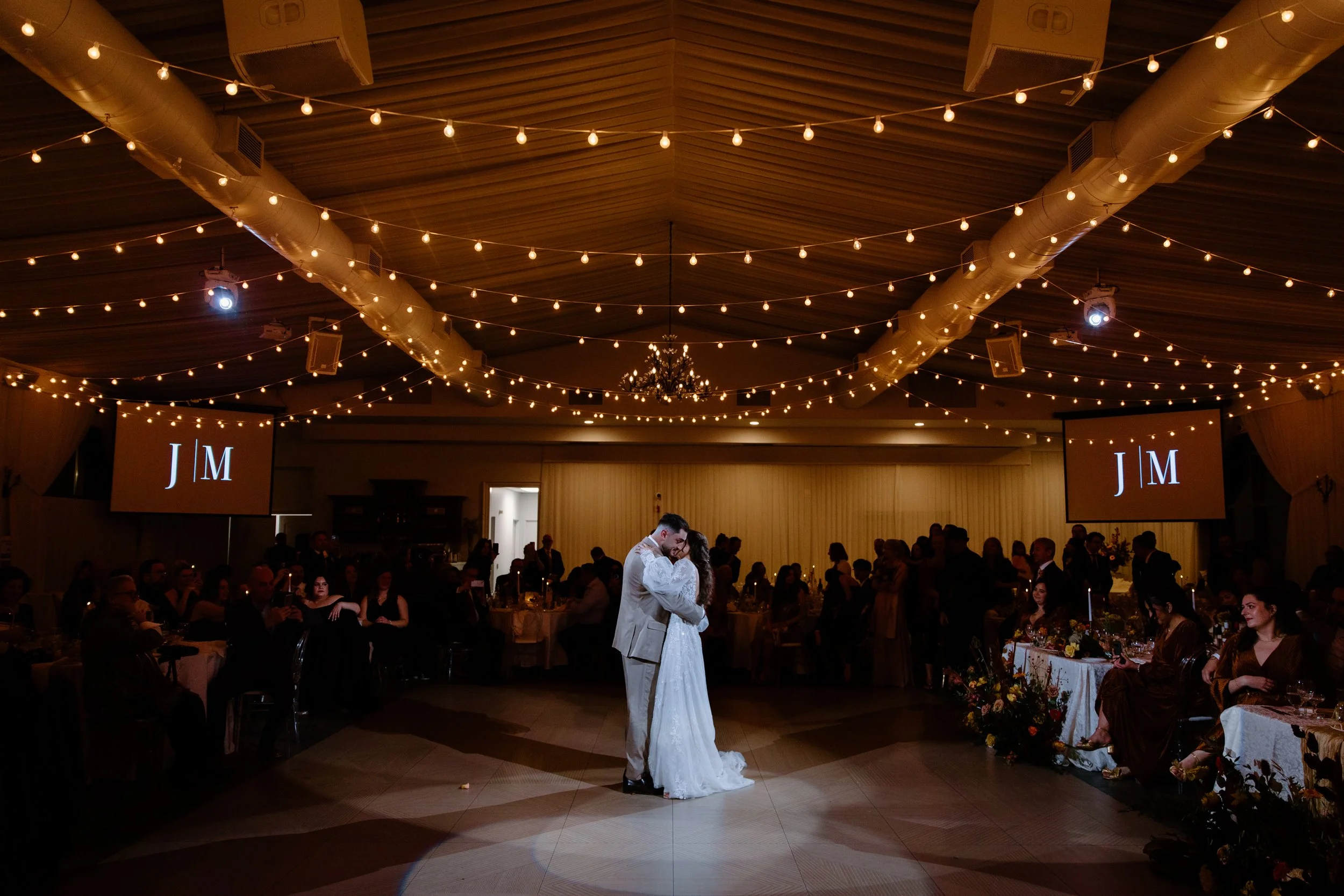 Wide room photo of a bride and groom sharing their first dance under a spotlight and twinkle lights at their Caledon wedding reception
