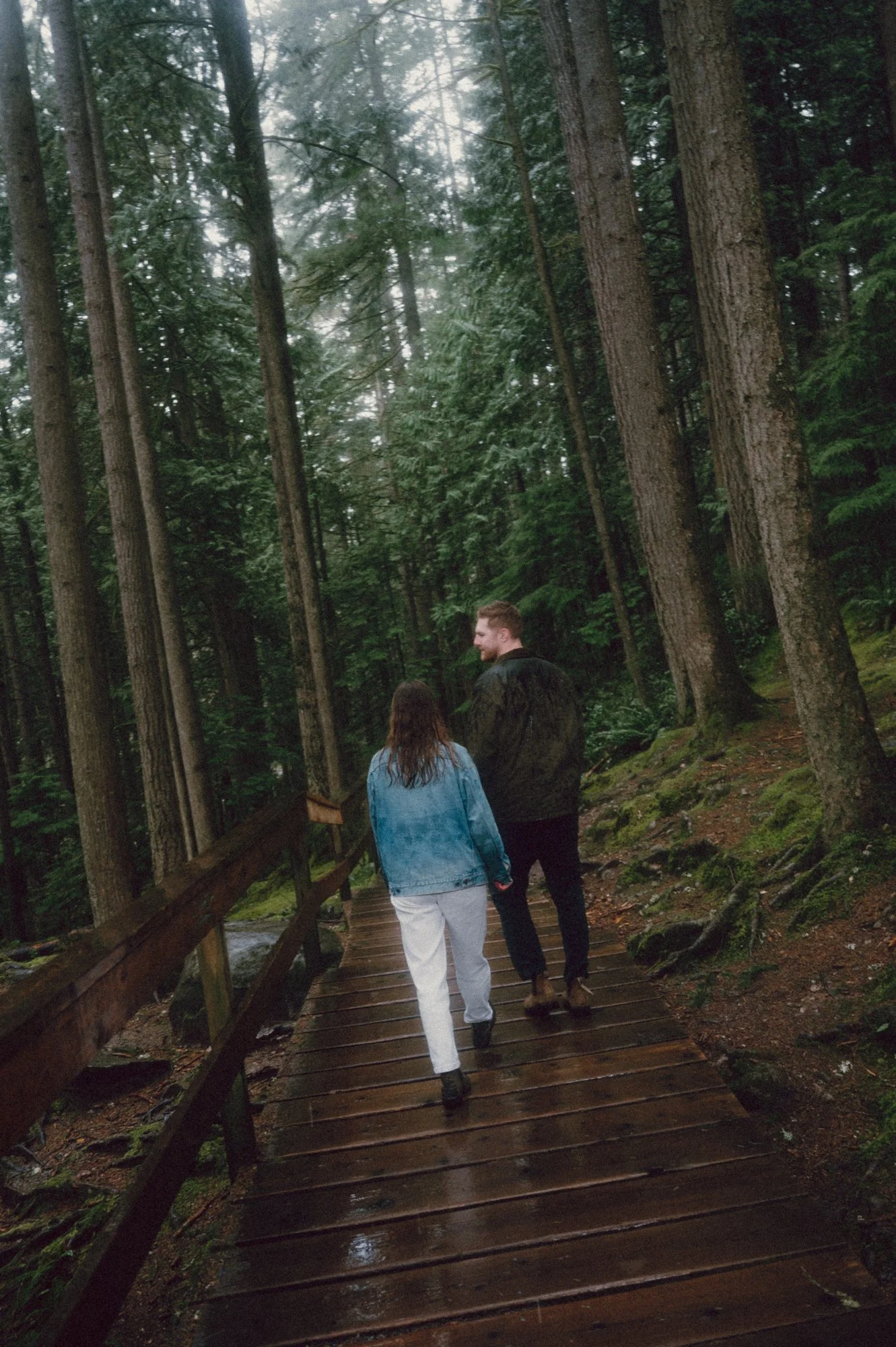 Candid film flash photograph of a couple walking along a forest boardwalk in Lynn Valley, North Vancouver, backs to the camera