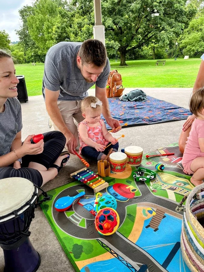 Babies and toddlers dancing and playing instruments at an outdoor music and movement playgroup in Kerr Park