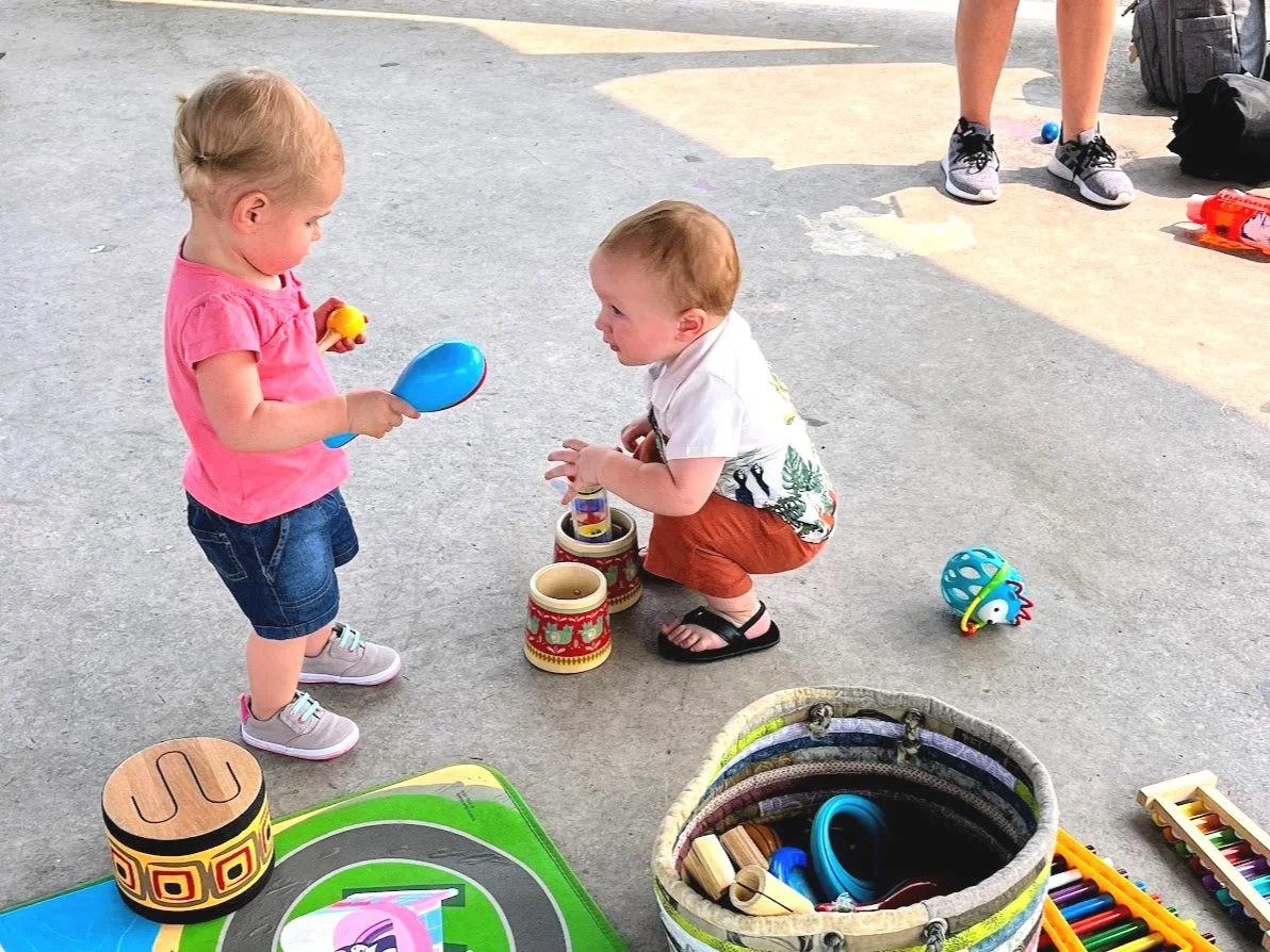 Babies and toddlers dancing and playing instruments at an outdoor music and movement playgroup in Kerr Park