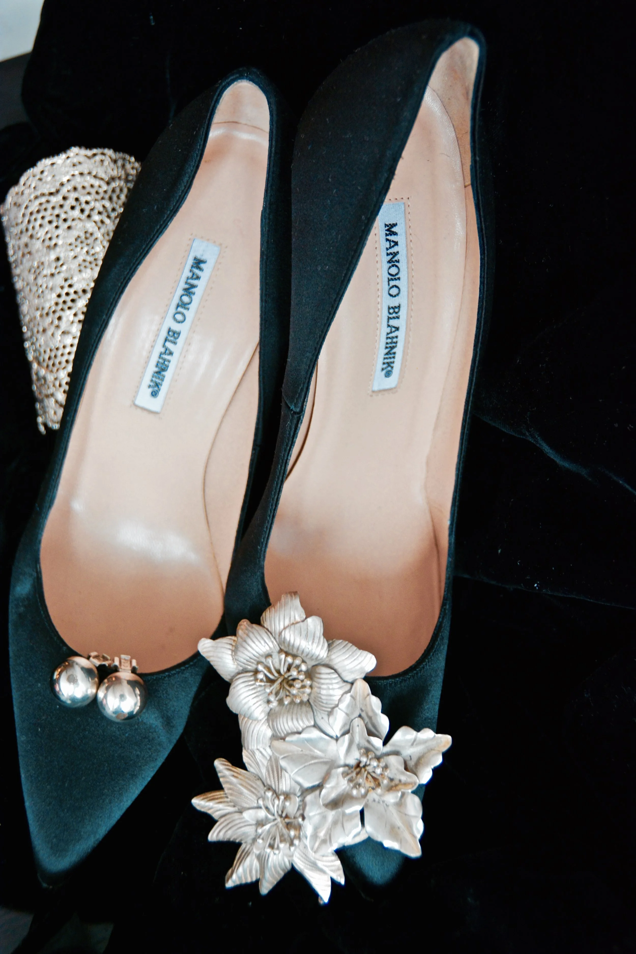 A pair of clip-on earrings adorns one shoe, while a silver brooch adorns the other.