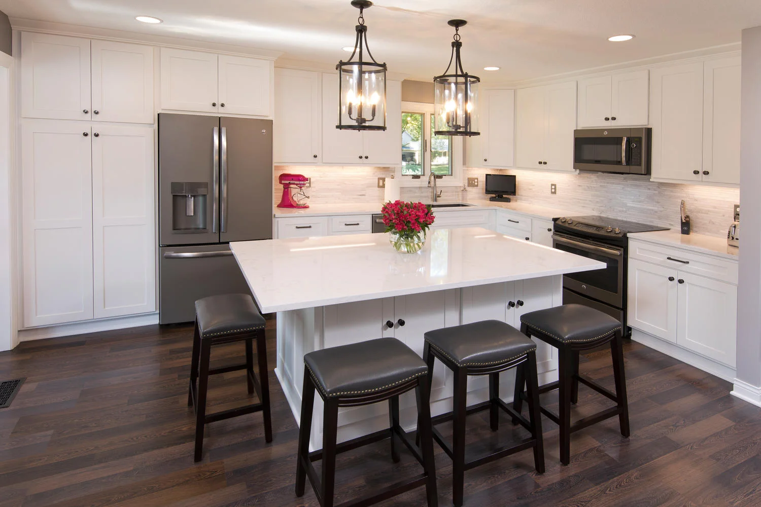 Bright, white kitchen with dark wood plank floors and island with quartz countertops and bar stools