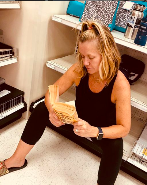 Still life with mother, reading The Thorn Birds whilst her tweens acquire school supplies.