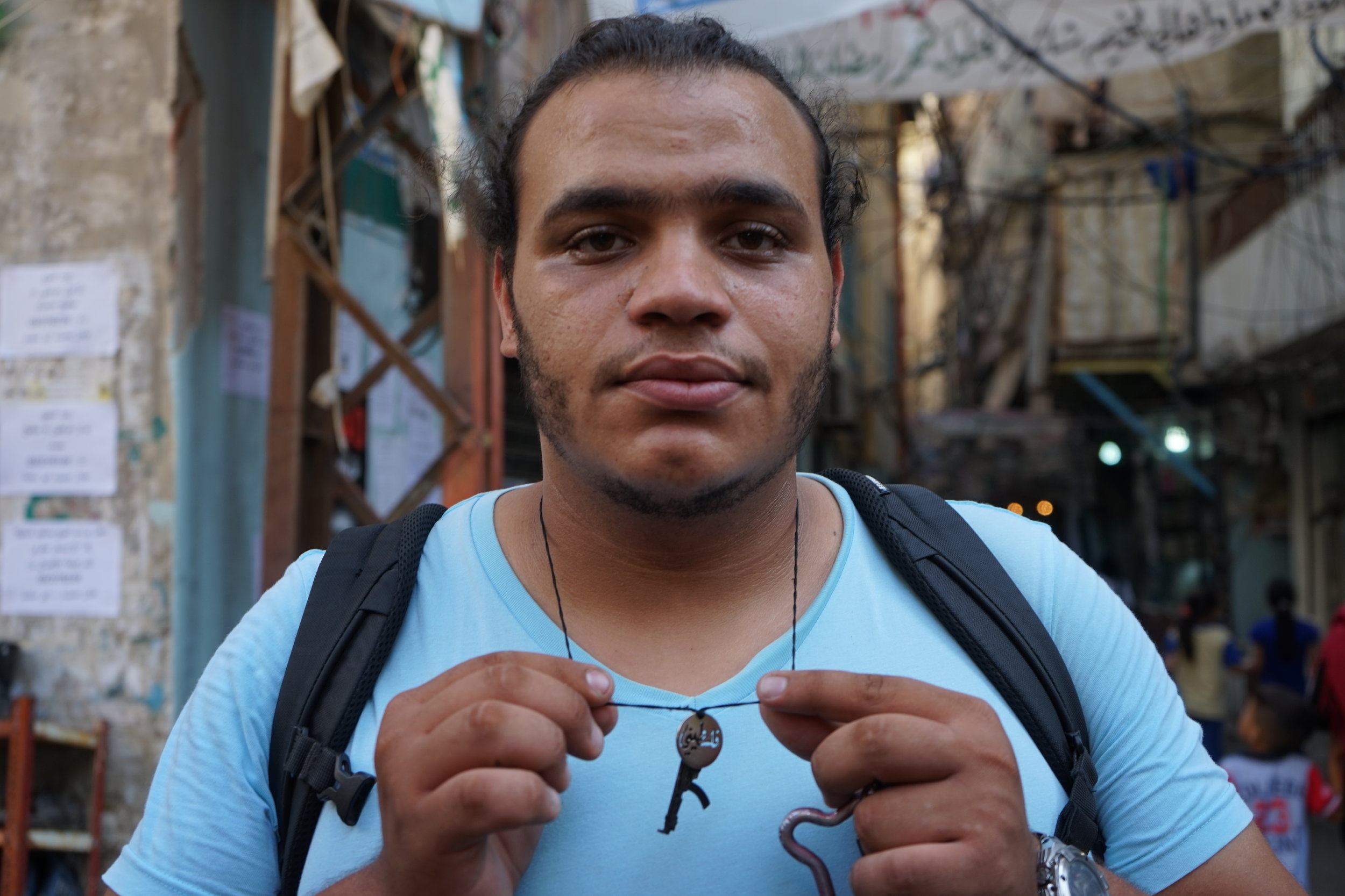  Abed Halimeh holds up his necklace,&nbsp;one charm reading "Palestine" in Arabic, the other a Kalashnikov, and the last in the shape of Handala, on August 18, 2016. 