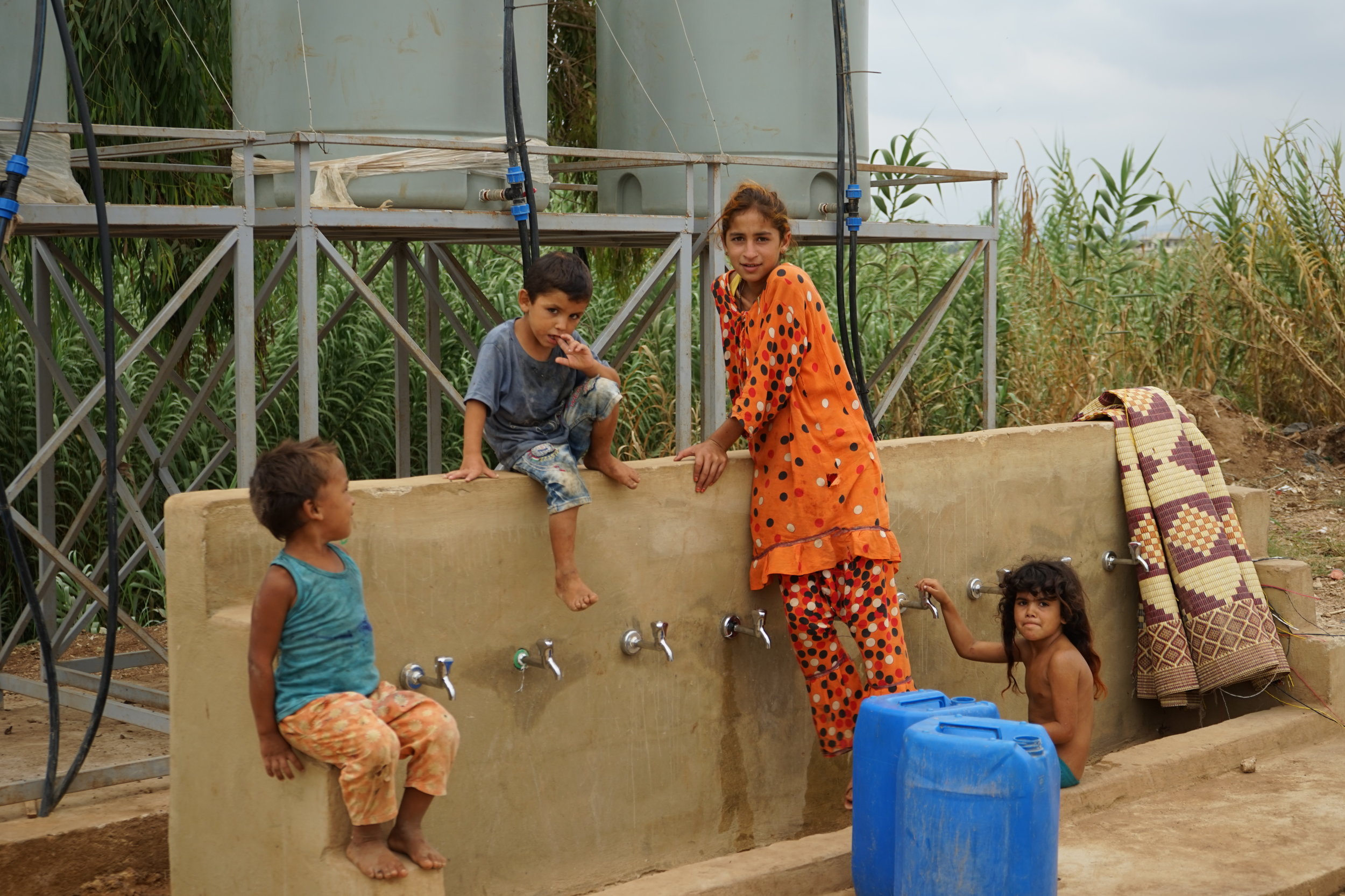  Children sit around a water well in UNHCR Syrian refugee camp 054 in 'Akkar on August 24, 2016. 