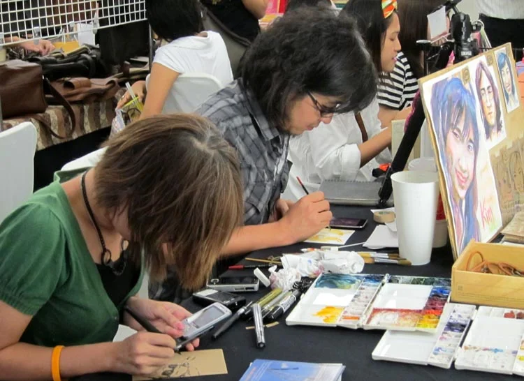 Artists working live at their stall. Painting from cell phones is a convenient way to let your portrait model keep shopping.