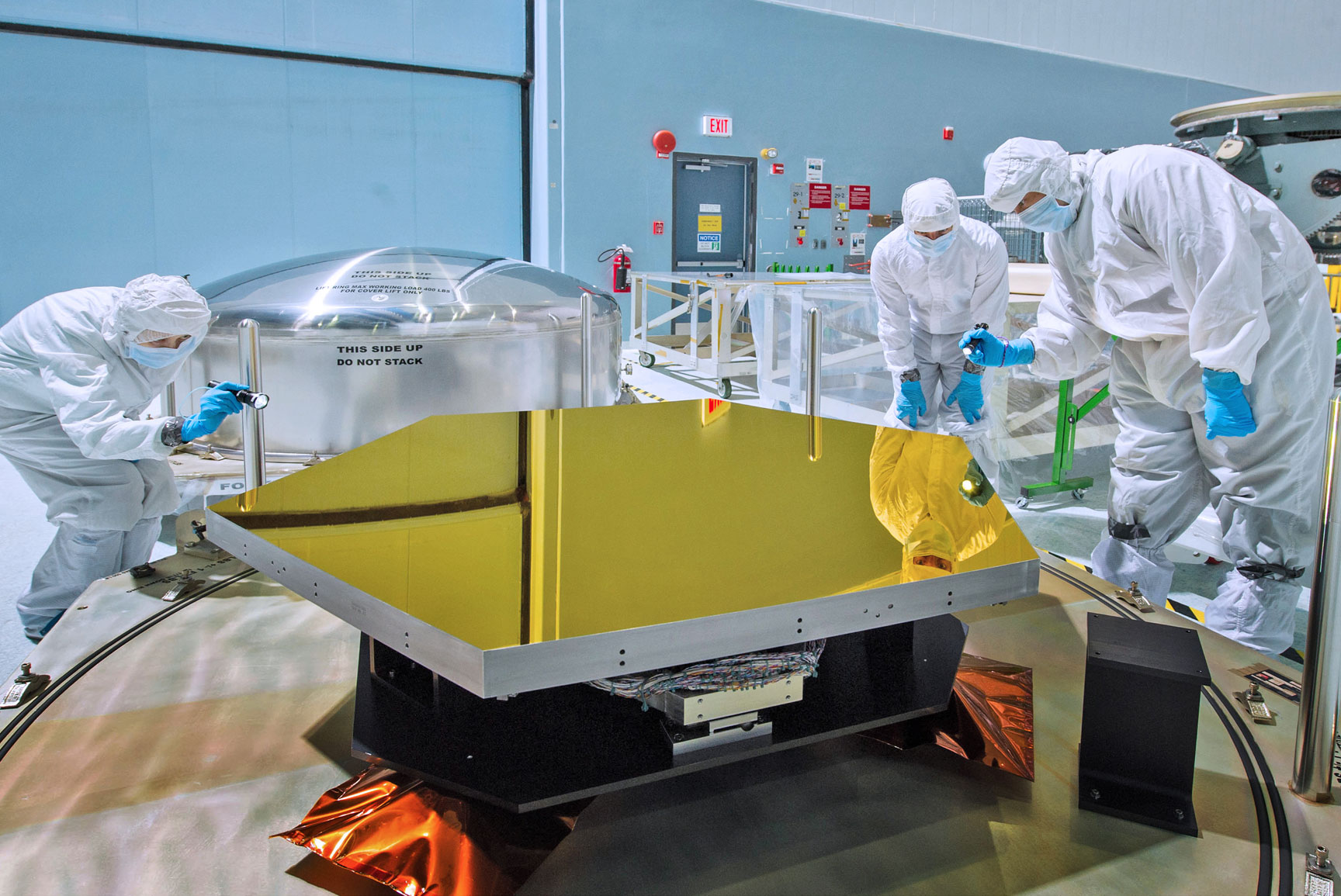 Technicians and scientists check out one of the Webb telescope’s first two flight mirrors in the clean room at NASA’s Goddard Space Flight Center in Greenbelt, MD. Credit: NASA/Chris Gunn