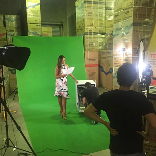 Using a green screen for an advertising video production. A woman holding a script with a dishwasher, and other crew in the back and foreground.
