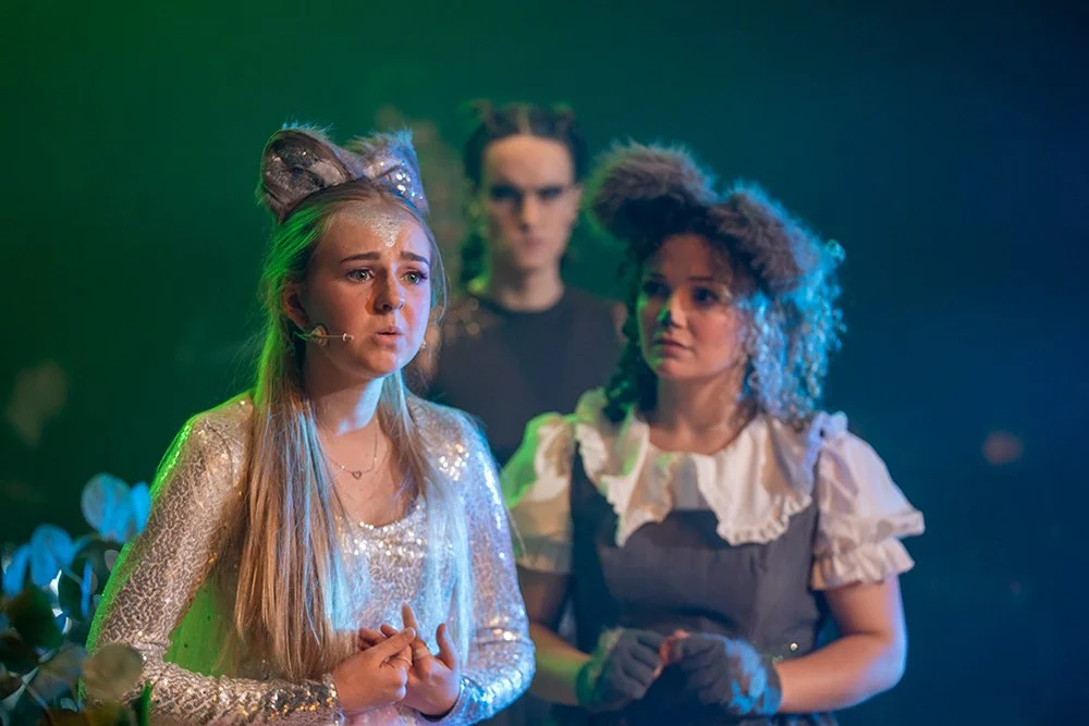 Theatre production with 3 actors on stage with dark green to dark blue background