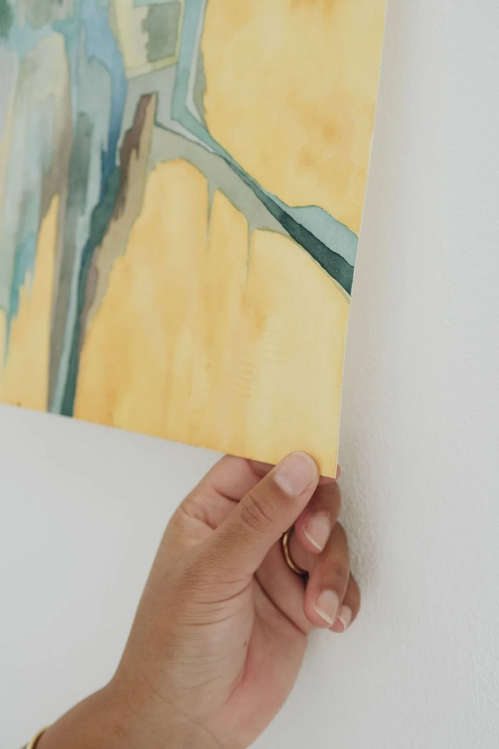 Close-up of a hand holding a colorful abstract painting against a white wall.