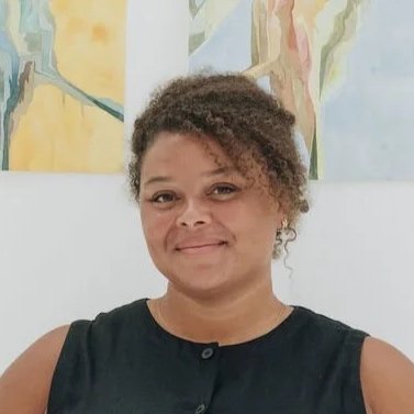 Woman with short curly hair wearing a sleeveless black top, standing in front of colorful abstract art.