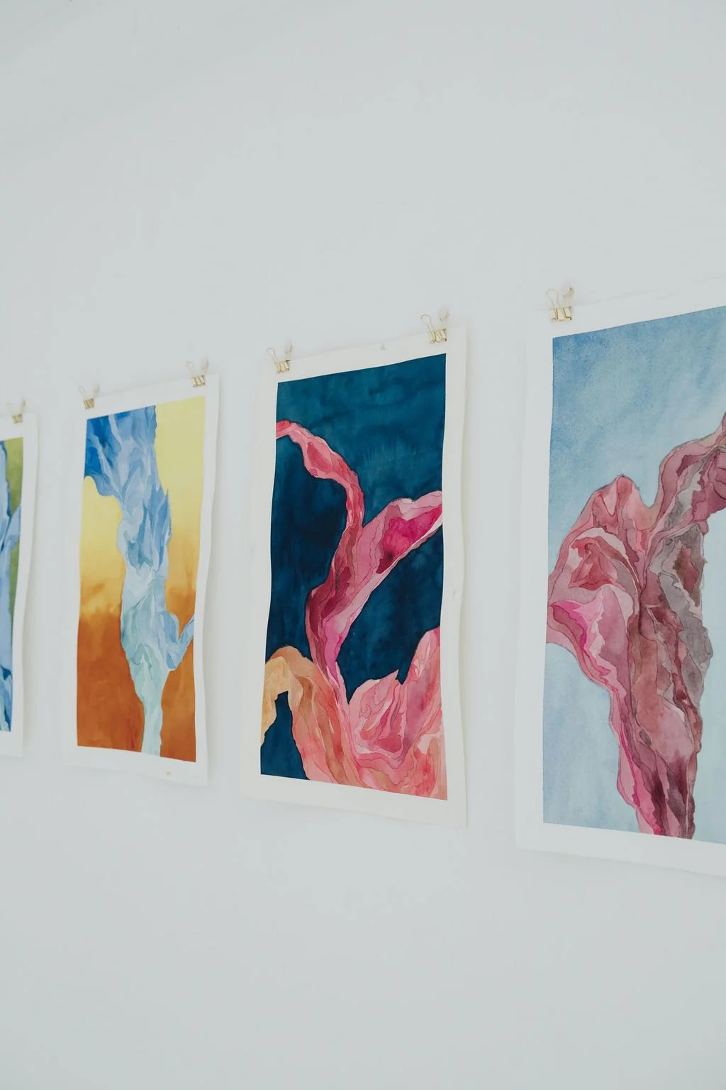 Watercolor paintings of abstract floral designs hanging on a white wall.