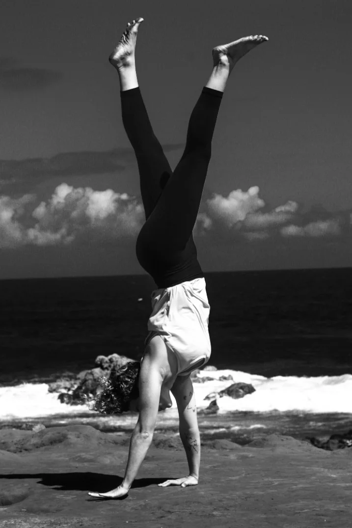 A person performing a handstand on the beach with ocean waves in the background, captured in black and white.