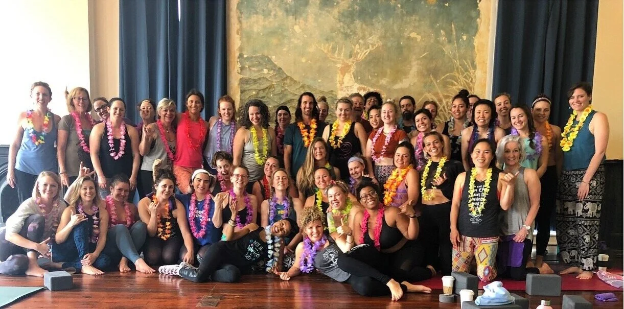 Group of women wearing colorful leis, smiling and posing together in a large room.