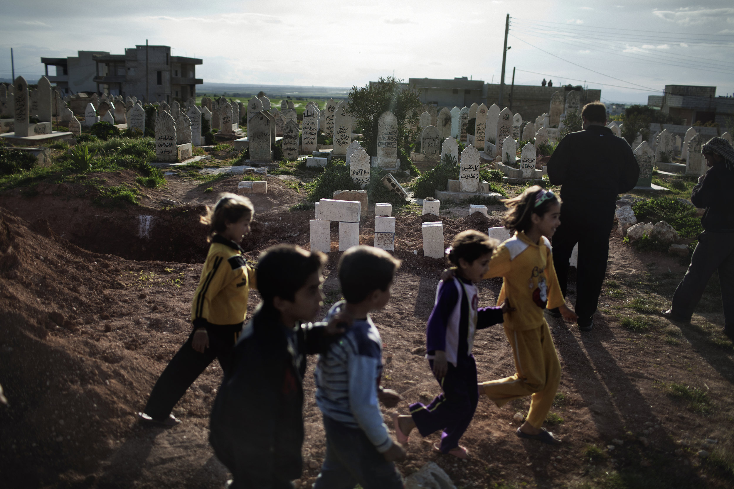  Children skip past a mass grave of victims of the massacre in Taftanaz.&nbsp; 
