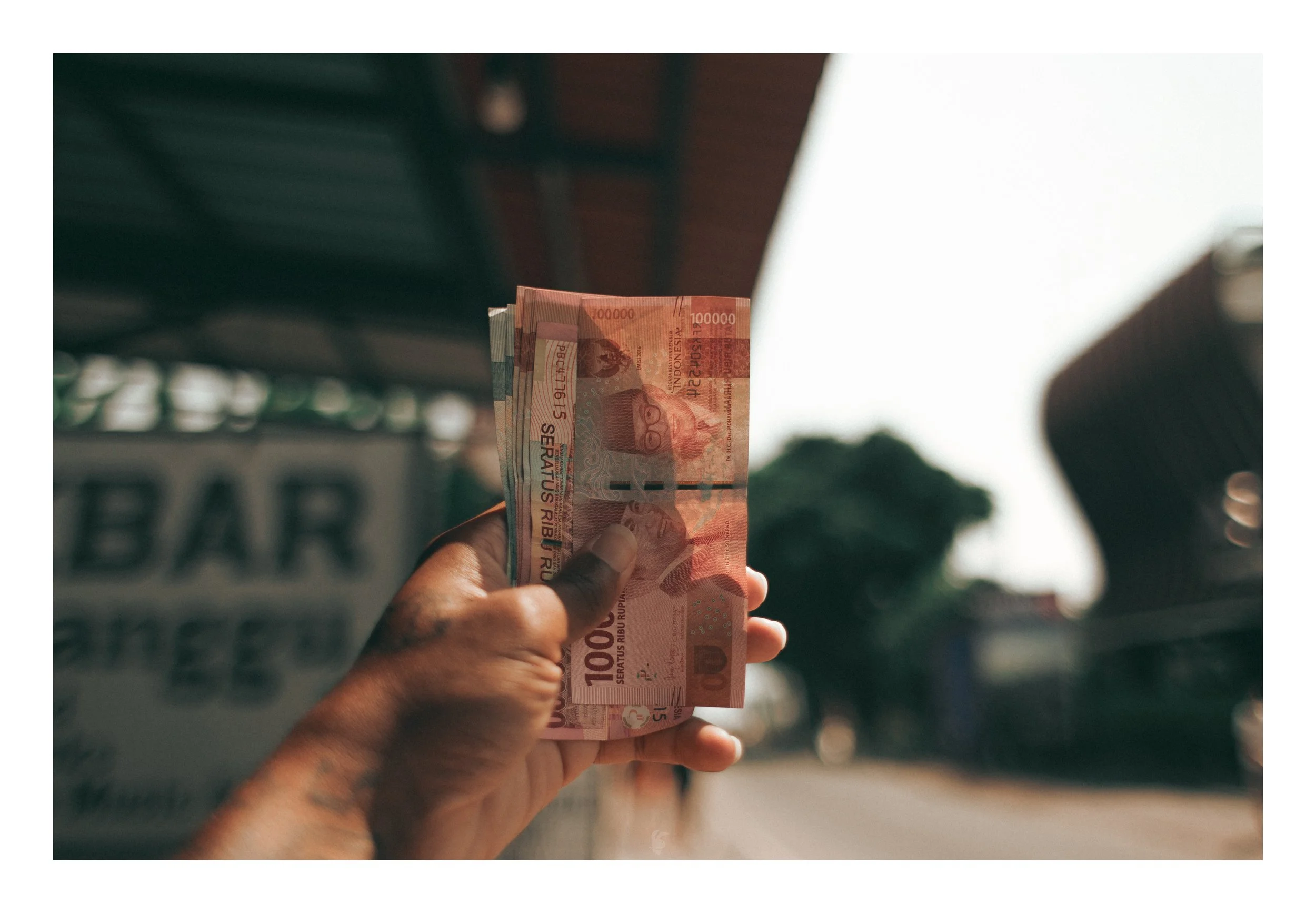 A person holding several 100,000 Colombian peso bills outdoors during daytime.