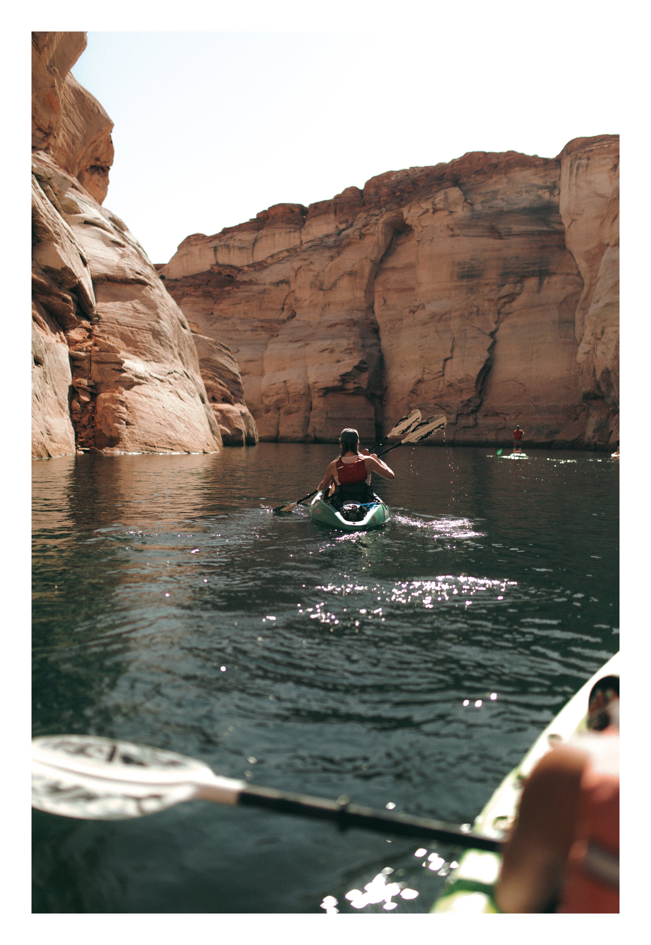 People kayaking on a river surrounded by tall sandstone cliffs in a desert landscape.