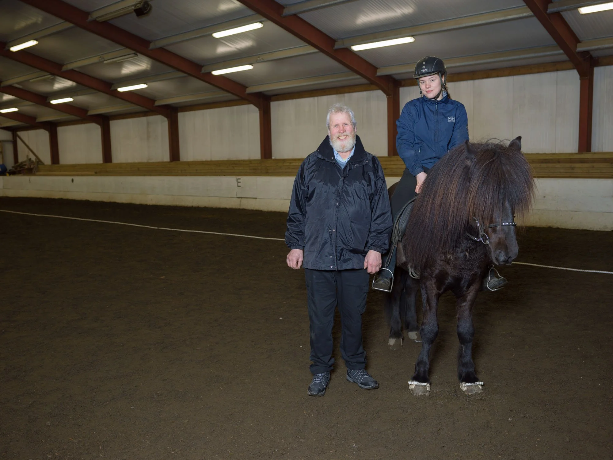 Child riding a horse beside a man inside an indoor arena