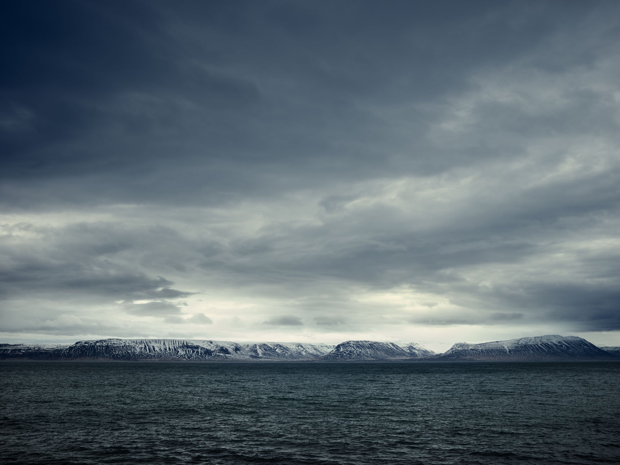 Snow-covered mountains across water beneath dark clouds