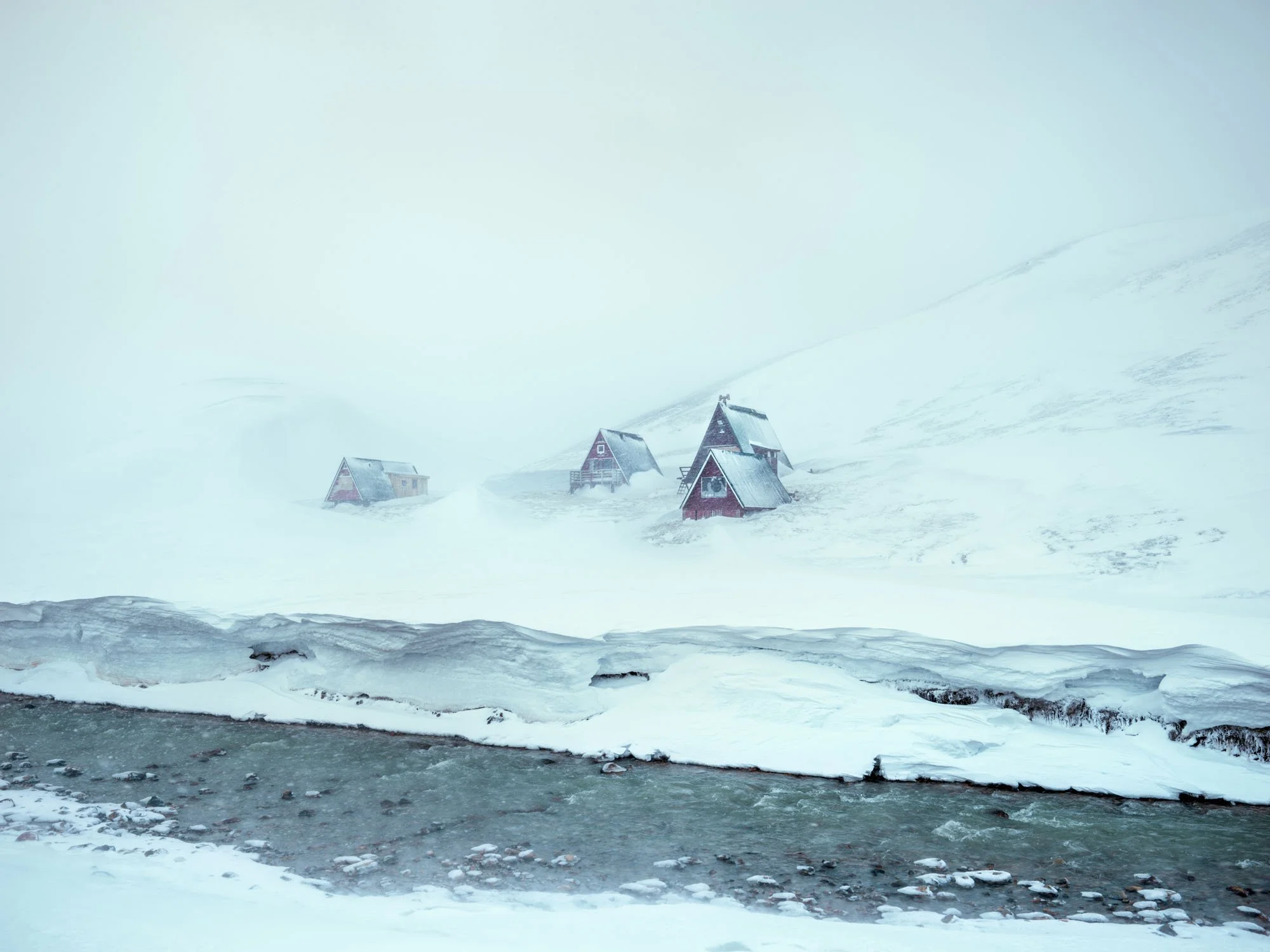 Three red houses on a snowy hillside beside a river