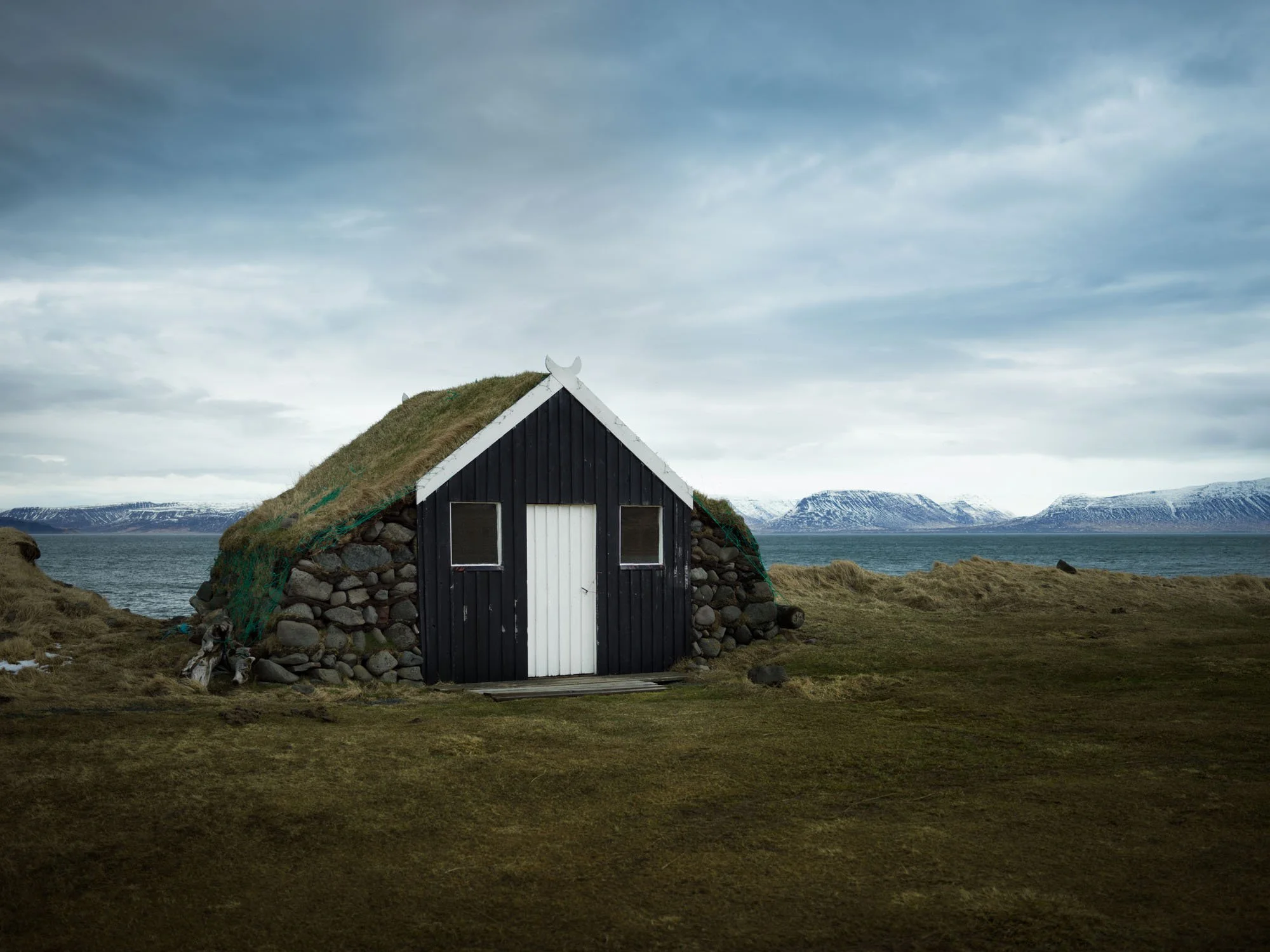 Black wooden house with a grass roof below the mountains
