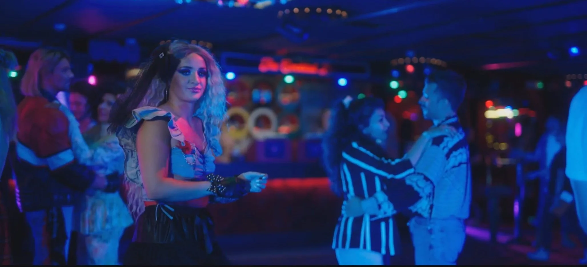 People dancing and socializing in a dimly lit nightclub with colorful neon lights.