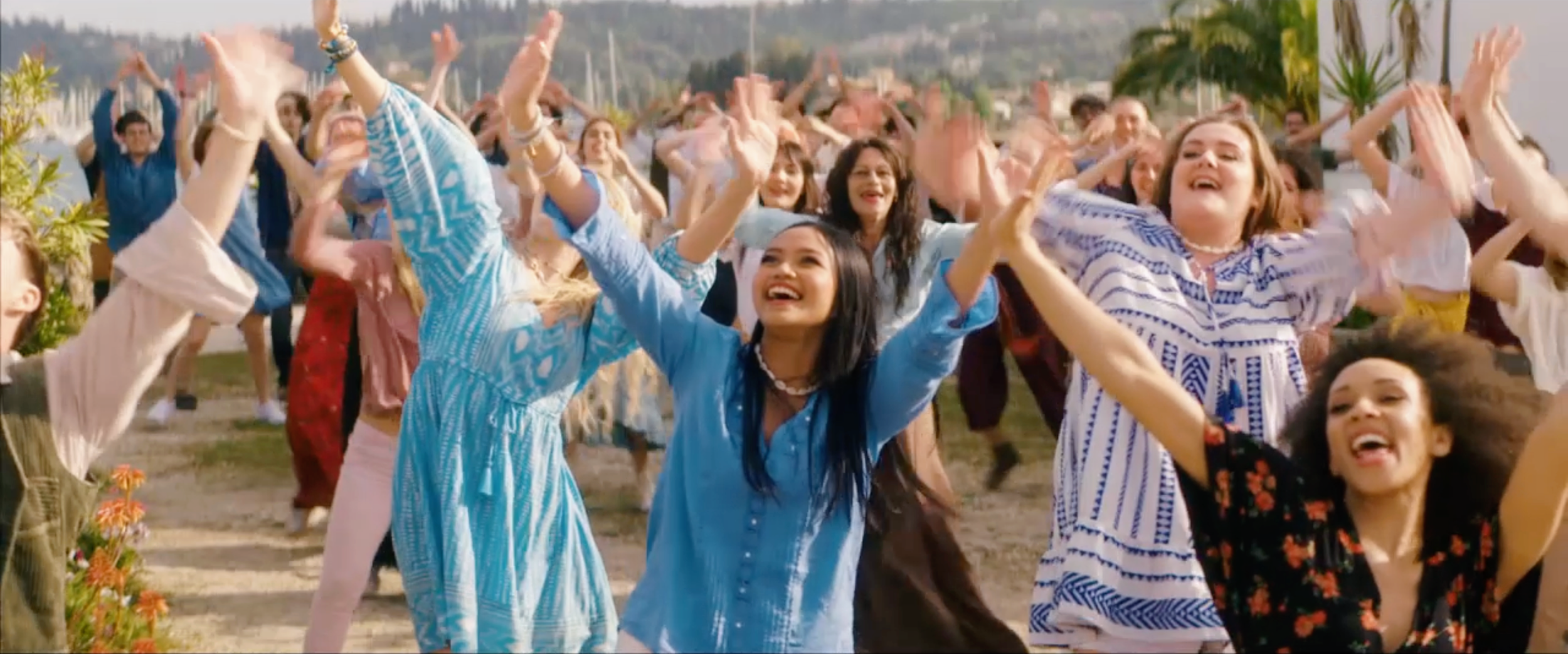 Group of diverse people dancing and celebrating outdoors during daytime.
