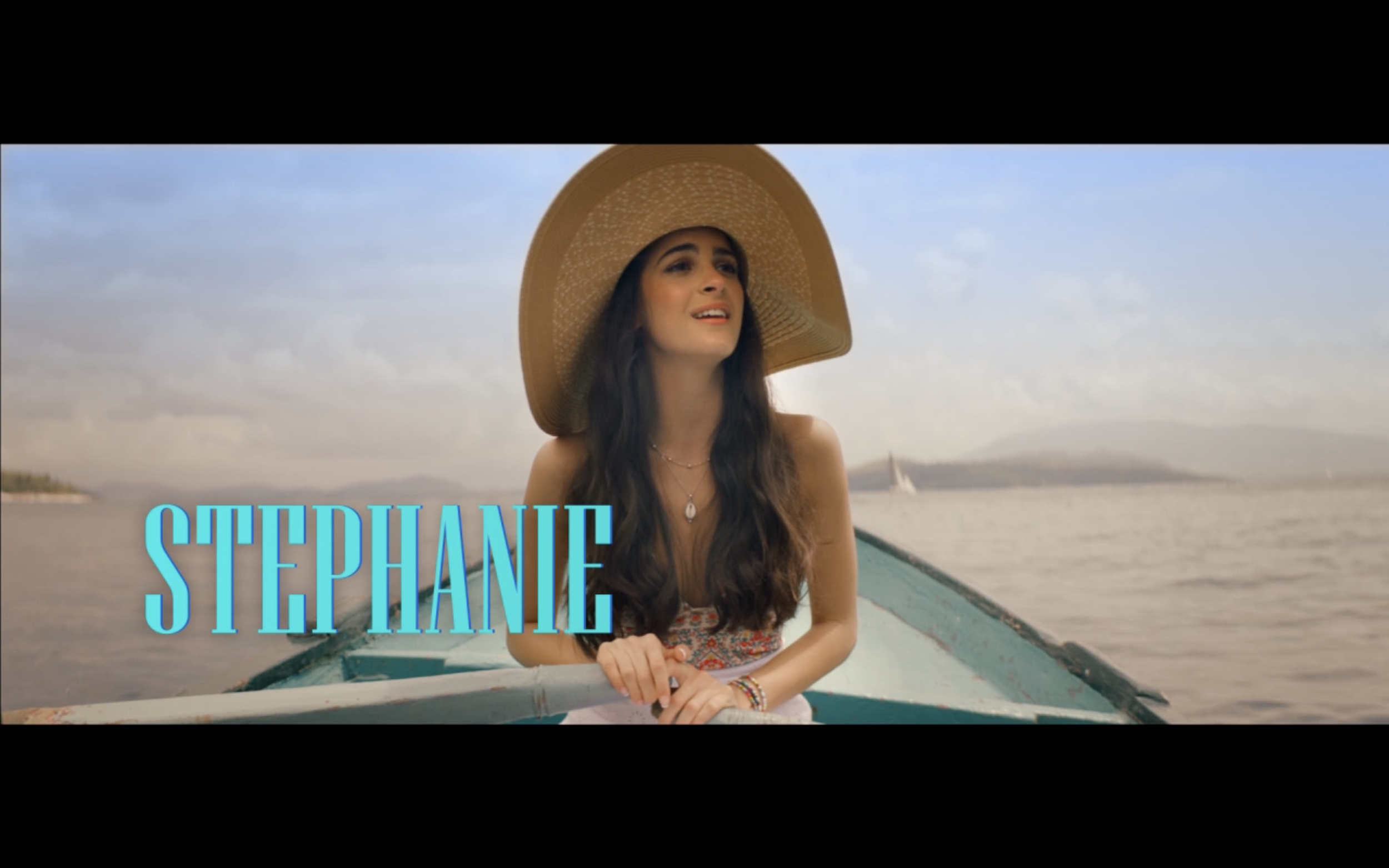 A woman wearing a large straw hat looks upward while sitting in a boat on a body of water, with a cloudy sky and distant shoreline in the background. The name 'Stephanie' is displayed in large blue letters.