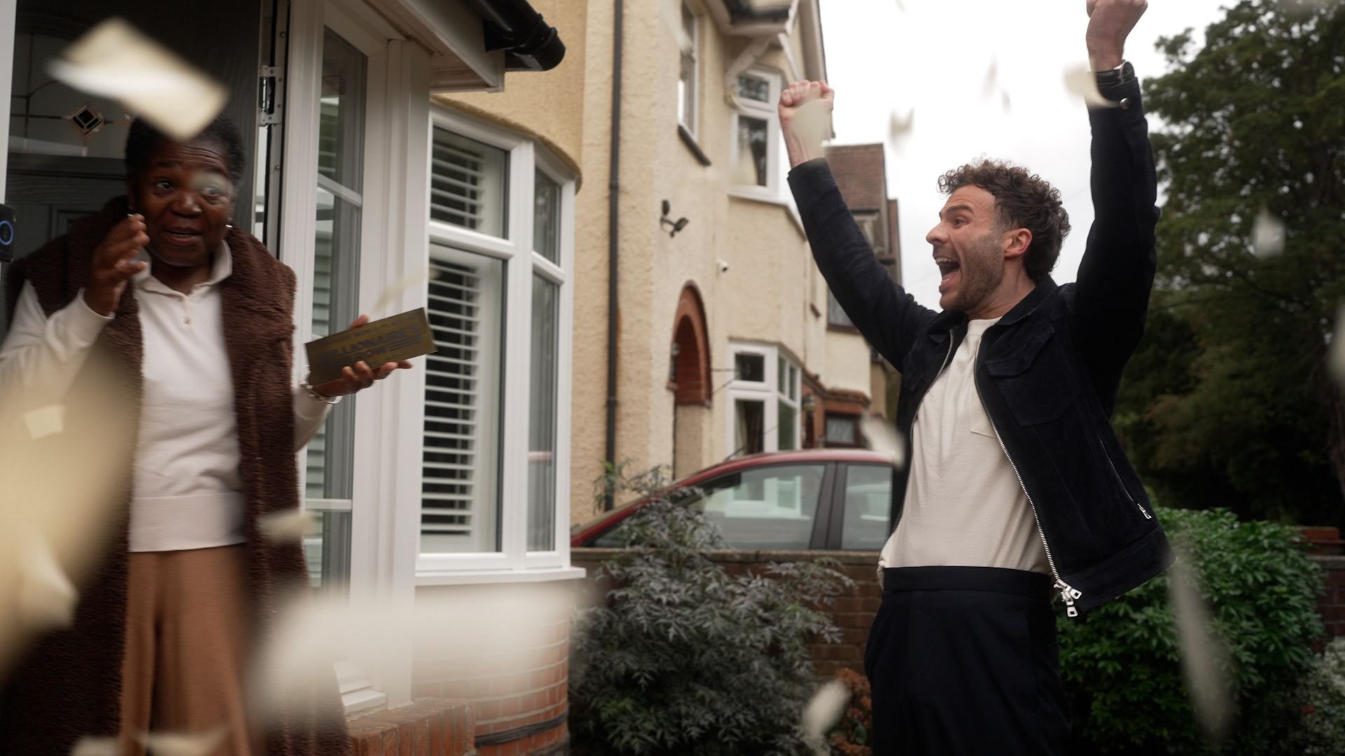 A man celebrating outside a house with her family as flowers fall around them.