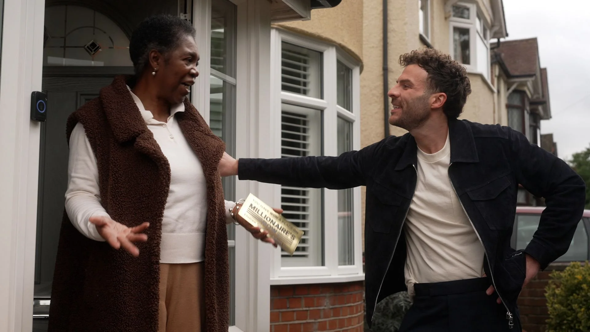 A man handing a woman a leaflet near a house, both smiling, during daytime.