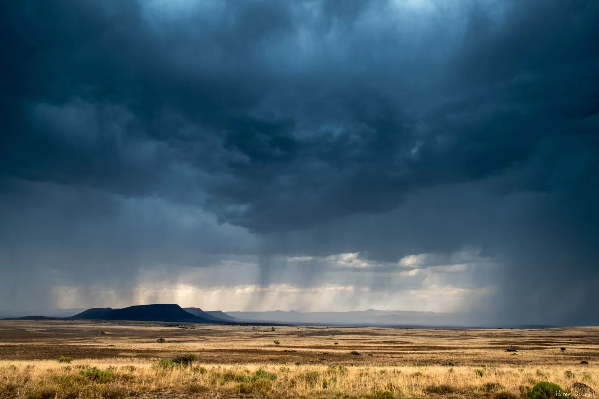 "Color photograph of a thunderstorm over the Karoo, South Africa. Dark clouds, lightning, and arid plains highlight the storm’s dramatic power."