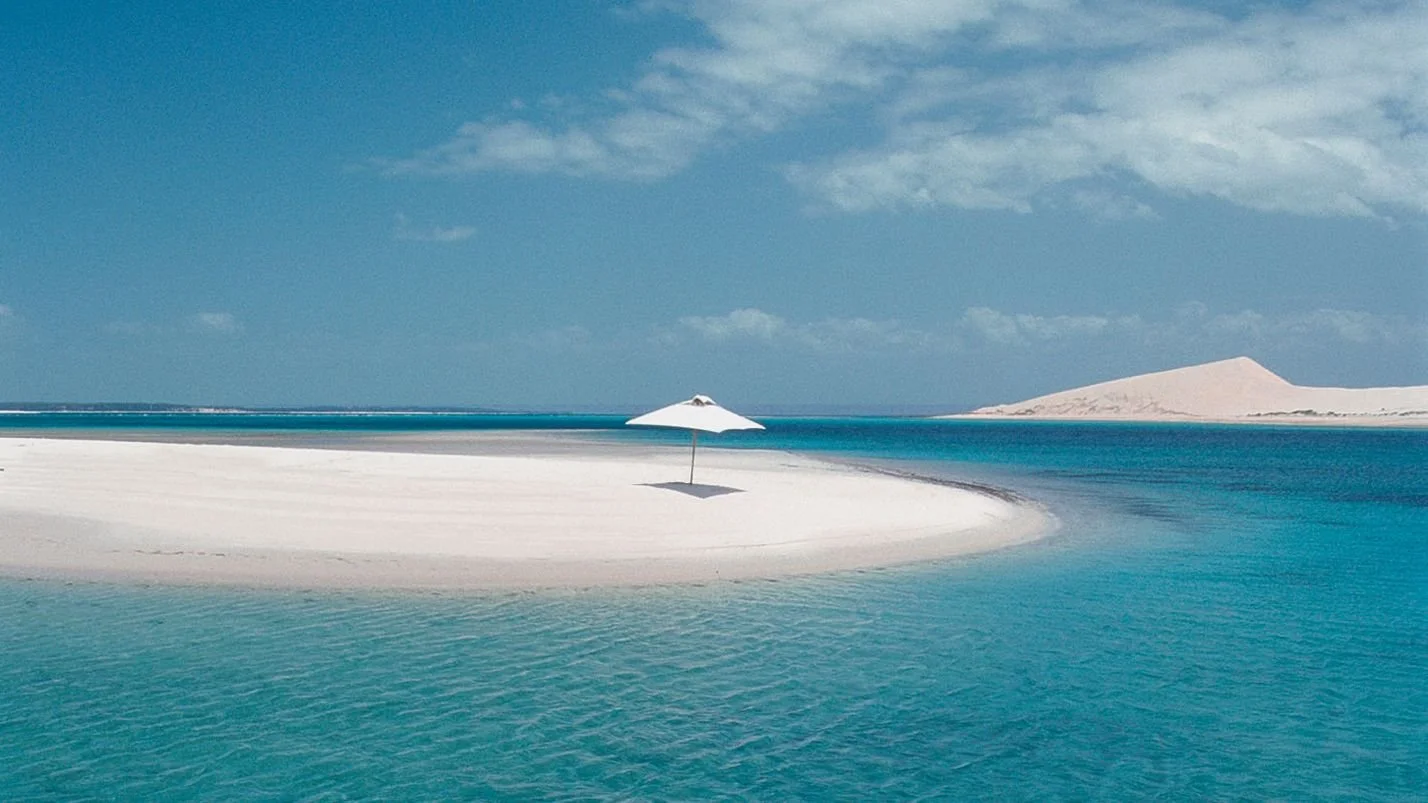 Pansy Island Mozambique with white sand dunes, Indian Ocean shoreline, and a single umbrella on an empty beach
