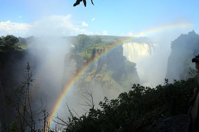 Victoria Falls in Zimbabwe with cascading water and a rainbow forming in the spray over the gorge