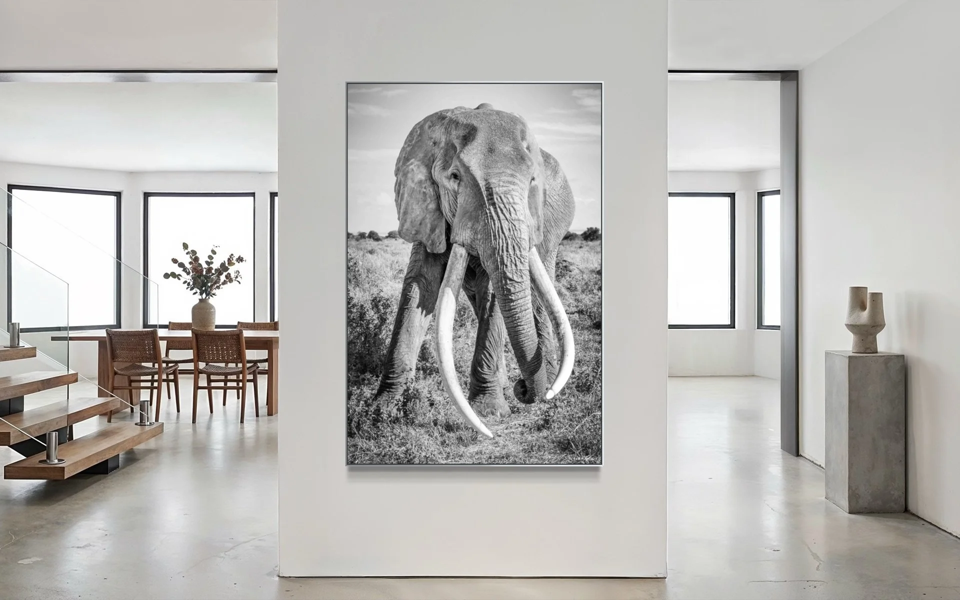 Craig the Super Tusker acrylic print on a narrow wall in a minimalist open-plan lounge with floating oak staircase and cement floors — black and white African wildlife art print by Peter Delaney.