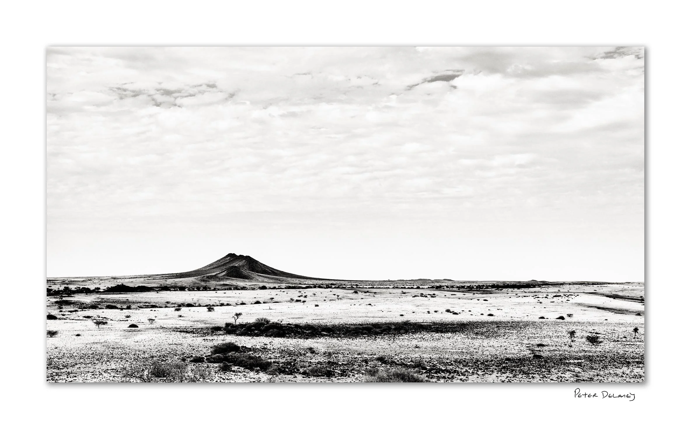 Black volcanic rocks with Spitzkoppe granite peaks in background — black and white fine art landscape print by Peter Delaney, Namibia