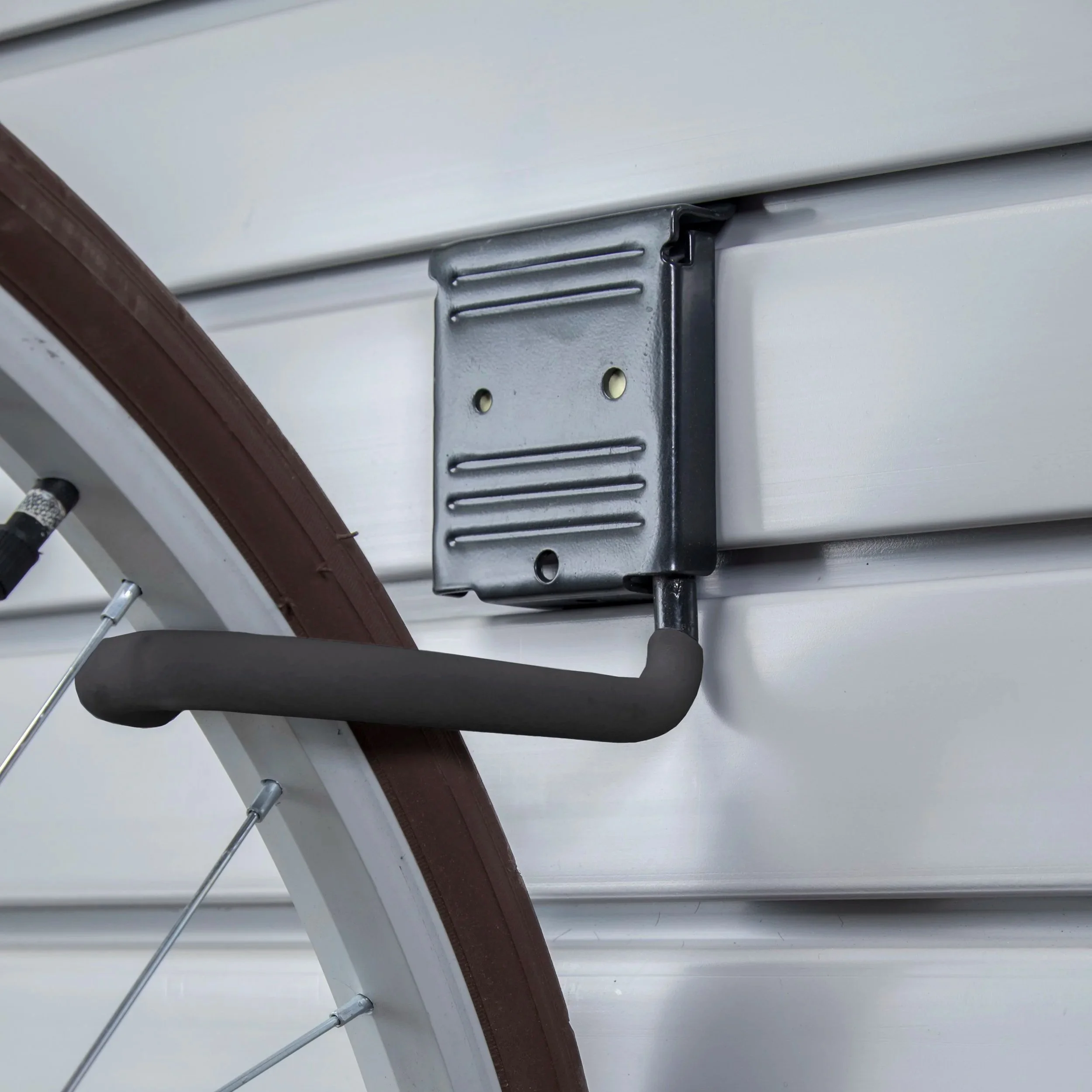  Seen up close, a black bike storage hook holds the wheel of a bicycle mounted vertically on a light grey slatwall.&nbsp; 