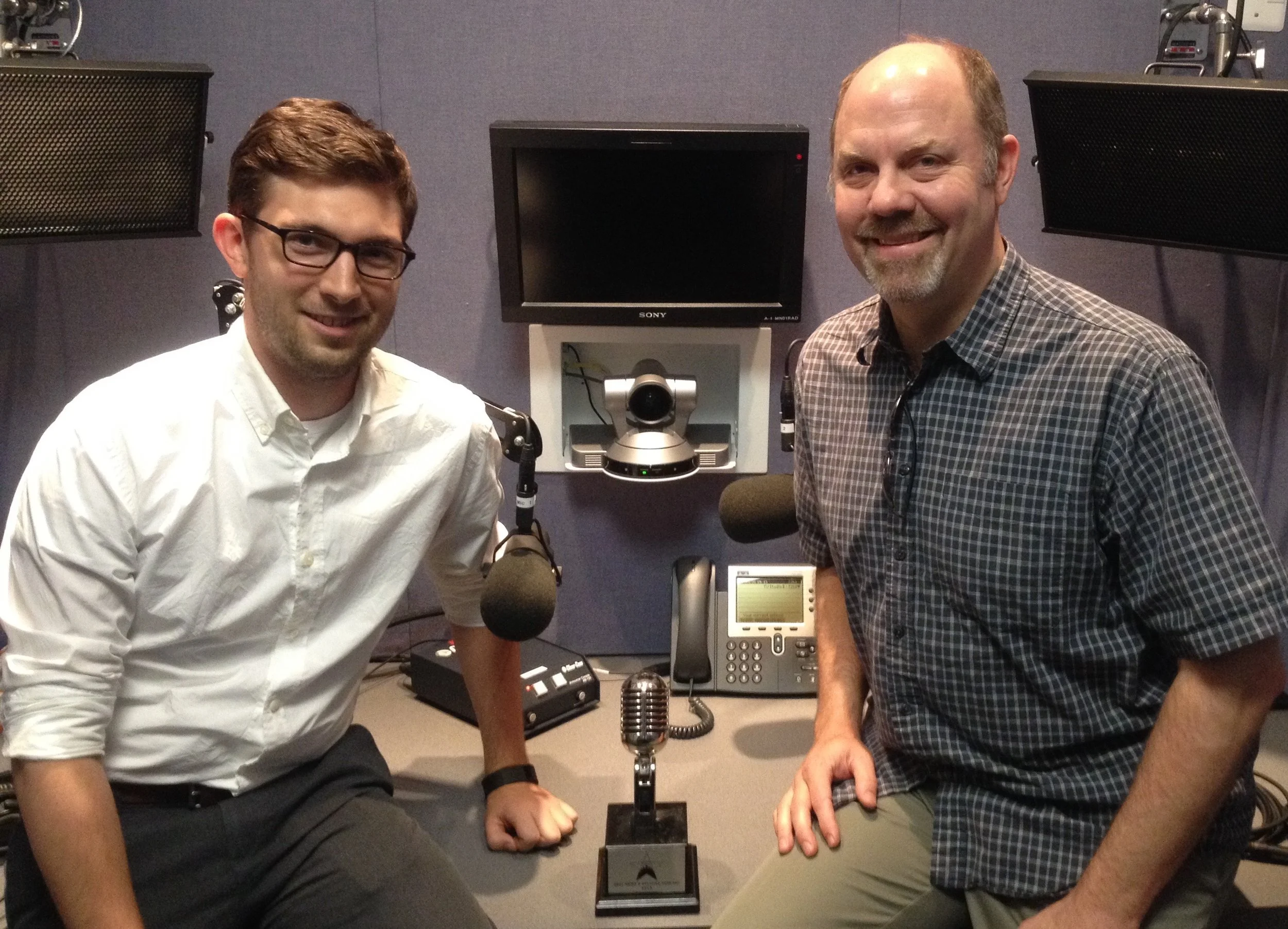 Zachary Kulzer and Fred Dews posing in the Brookings Radio Studio with the 2015 Podcast Movement Award for best News and Politics Podcast