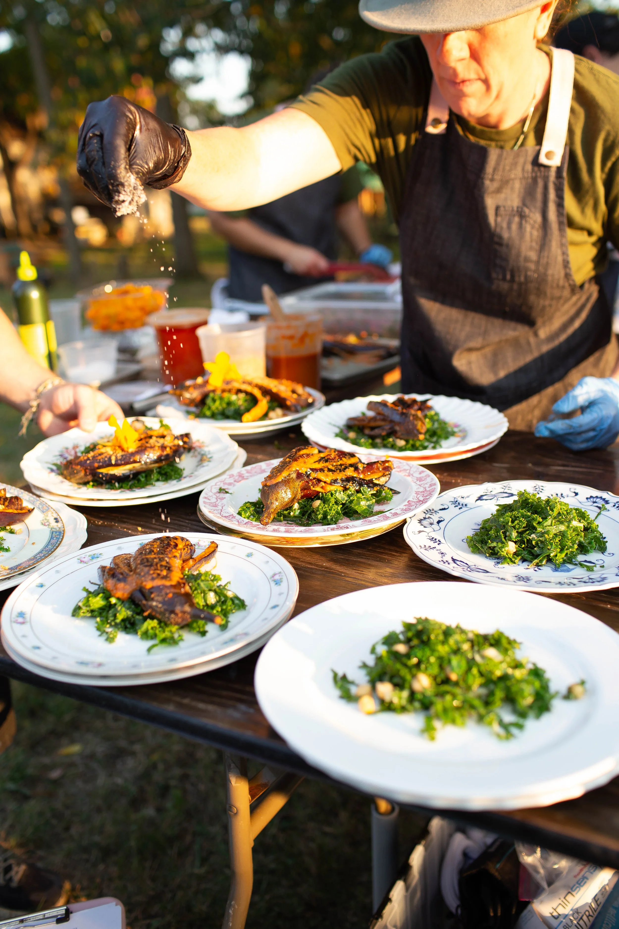 A caterer sprinkles salt onto a chicken plated on a salad outside.